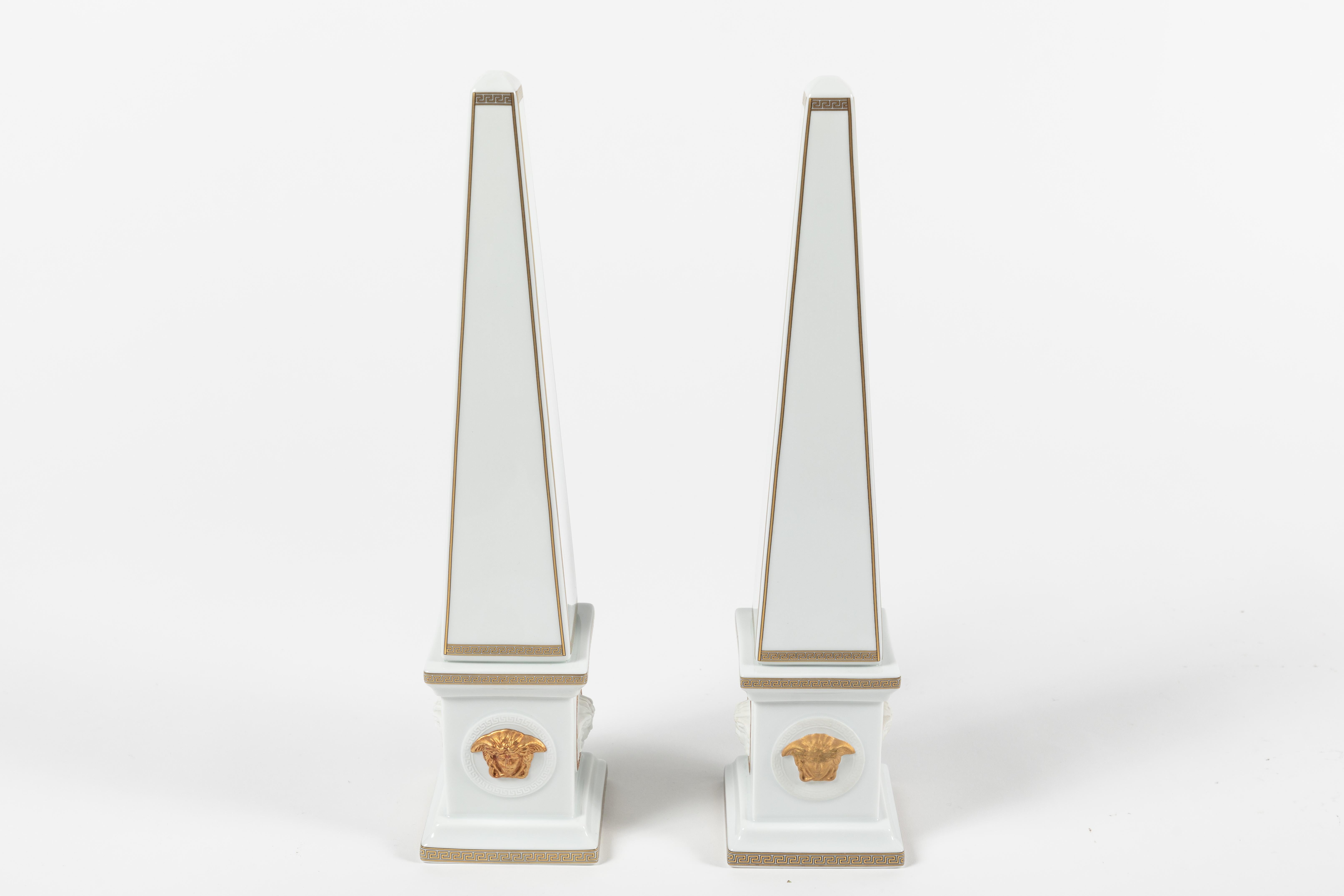 These are a pair of porcelain obelisks designed by Versace and produced by Rosenthal Germany. Four Versace logo medusa heads in gilt glaze grace the four sides of the base while the iconic Greek key pattern is decorated ornately around the edges.