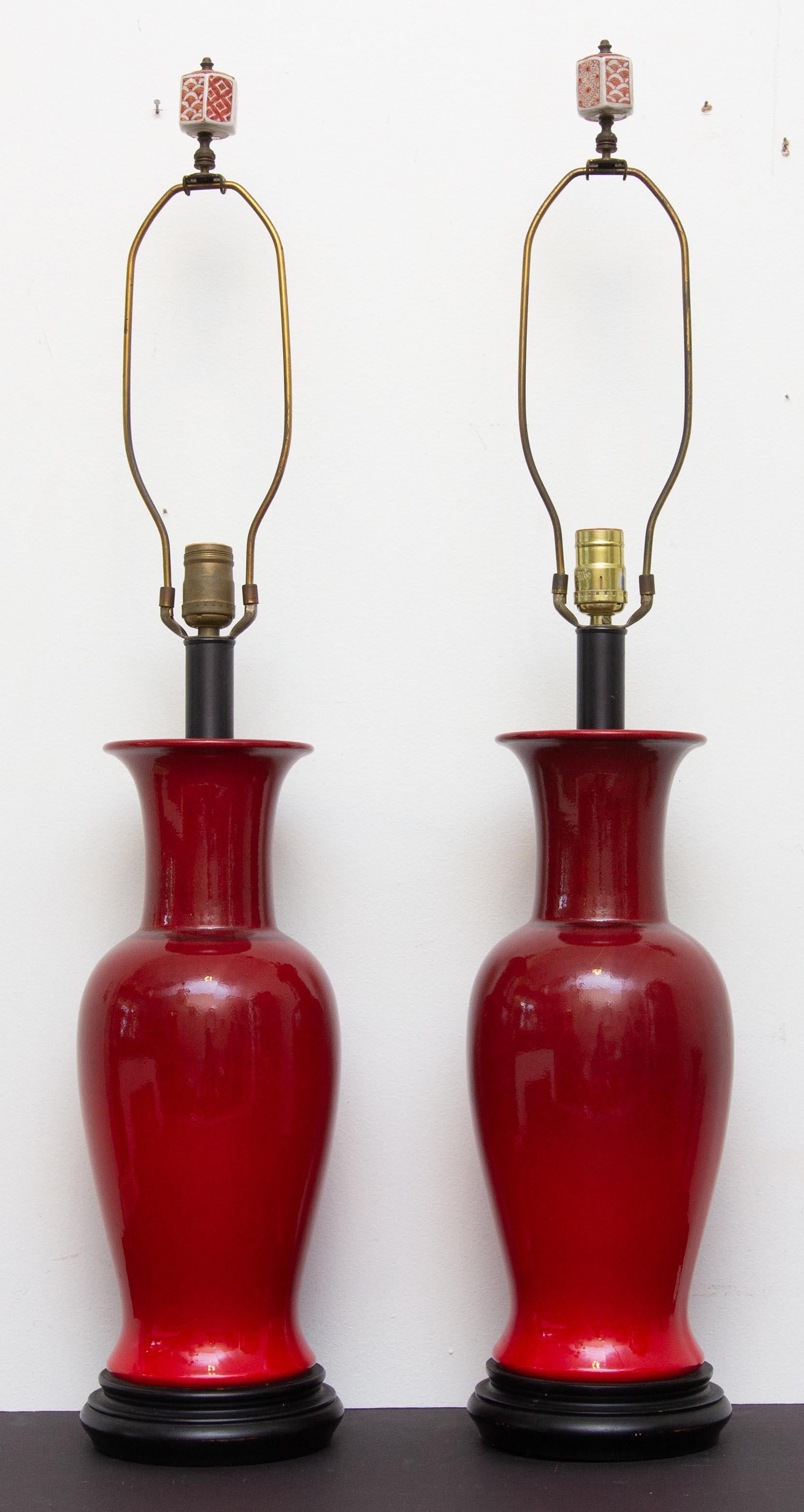 Pair of glazed porcelain sang de boeuf lamps. Oxblood color. Good porcelain finials, circa 1960s. Measures: Height to top of urns 18