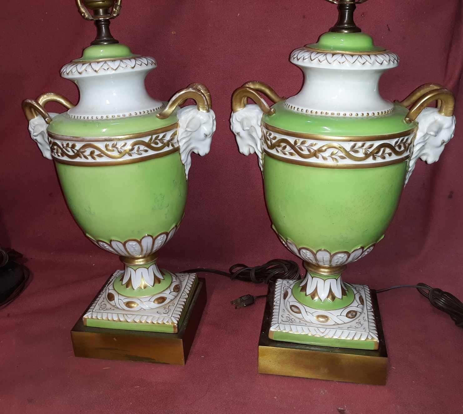A pair of gilt porcelain rams head motif lamps in light Peridot green. The urn form with ram head handles on a square brass base.