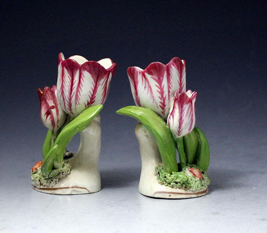A highly decorative pair of tulip ornaments the main flower modelled with leaves and buds on a circular base with a single flower nestled on the grass.

Dimensions: 3.00 inch wide 3.75 inch high 2.00 inch deep

Medium: porcelaineous China