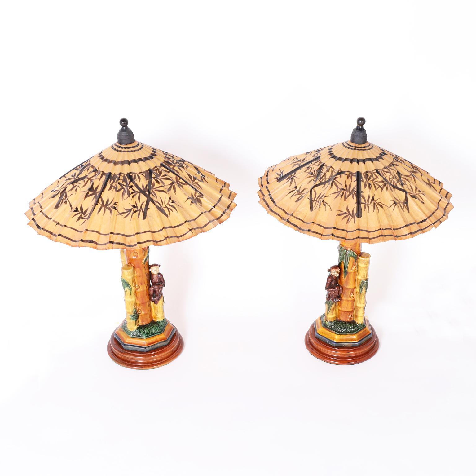 Pair of vintage Chinese table lamps with paper umbrella shades hand decorated and varnished over porcelain bamboo plants with monkeys on turned wood bases.