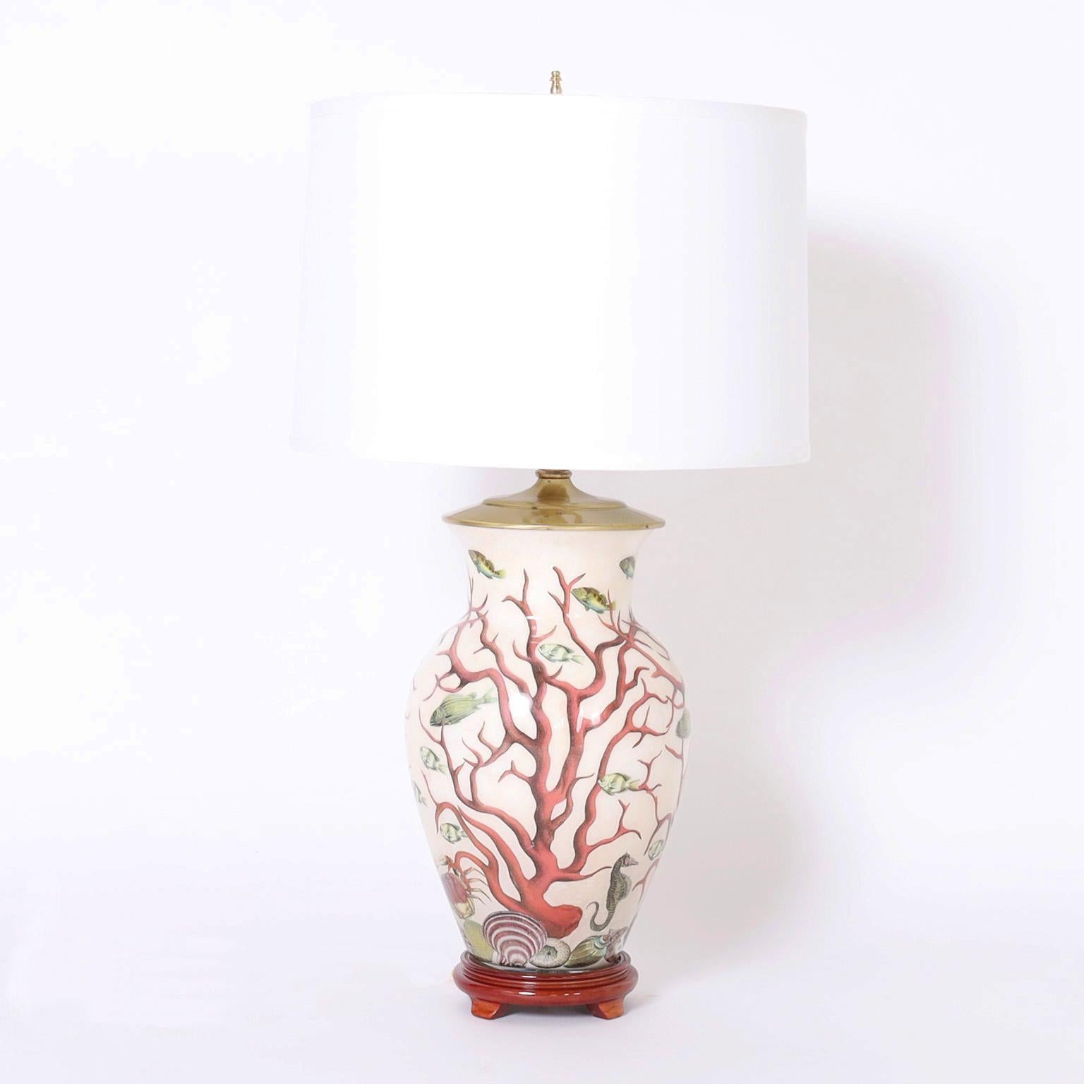 Standout pair of vintage table lamps crafted in porcelain in a classic form hand decorated in a sophisticated composition of red coral, fish, and seashells and presented on a turned wood base.
