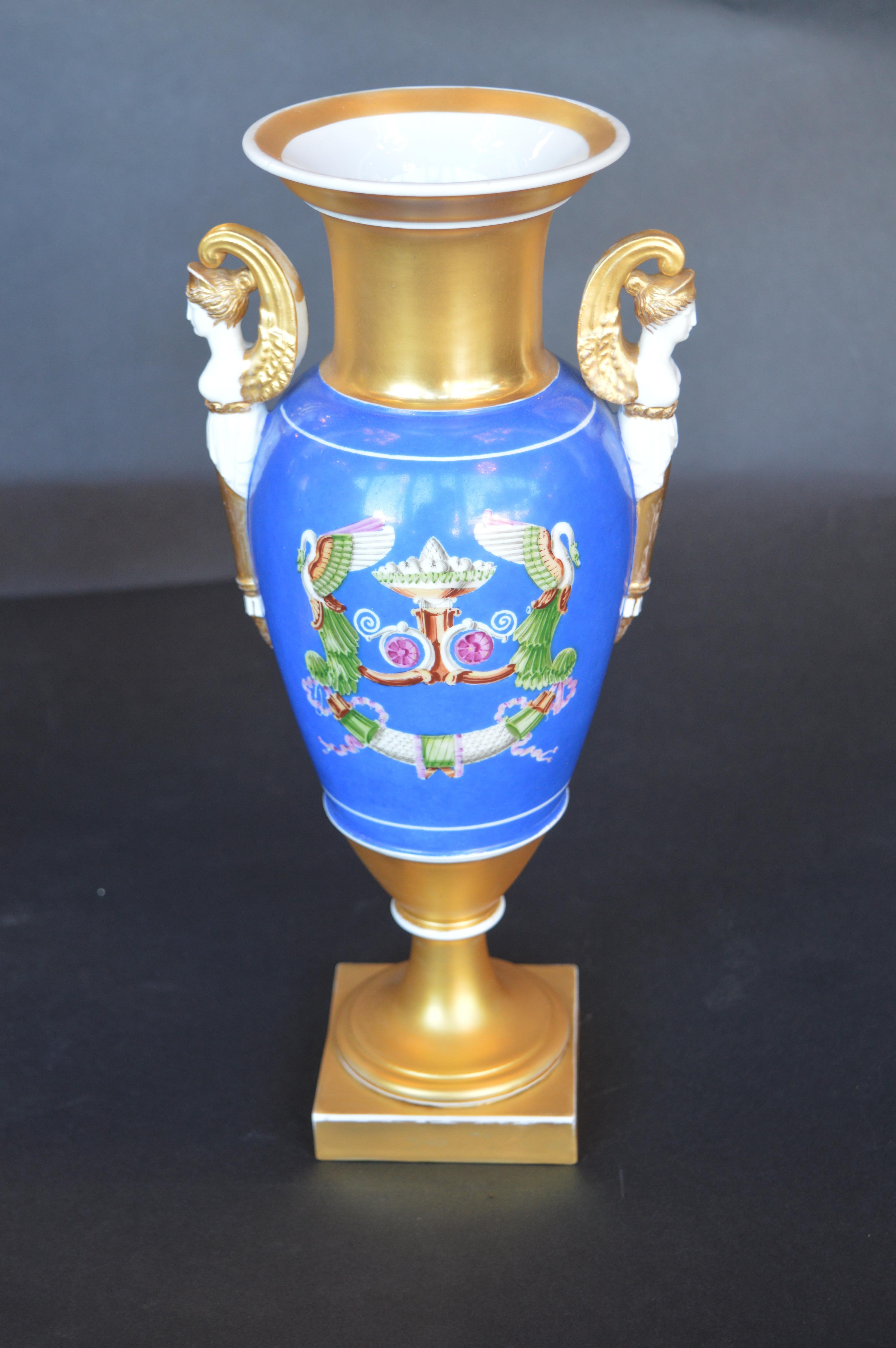 Coppia di vasi in porcellana con raffigurazioni in stile barocco dipinte a mano su un lato e stemmi dorati sull'altro. Ogni vaso è ornato da manici greci-romani dorati e rifinito con una pesante doratura lungo la base e il bordo.