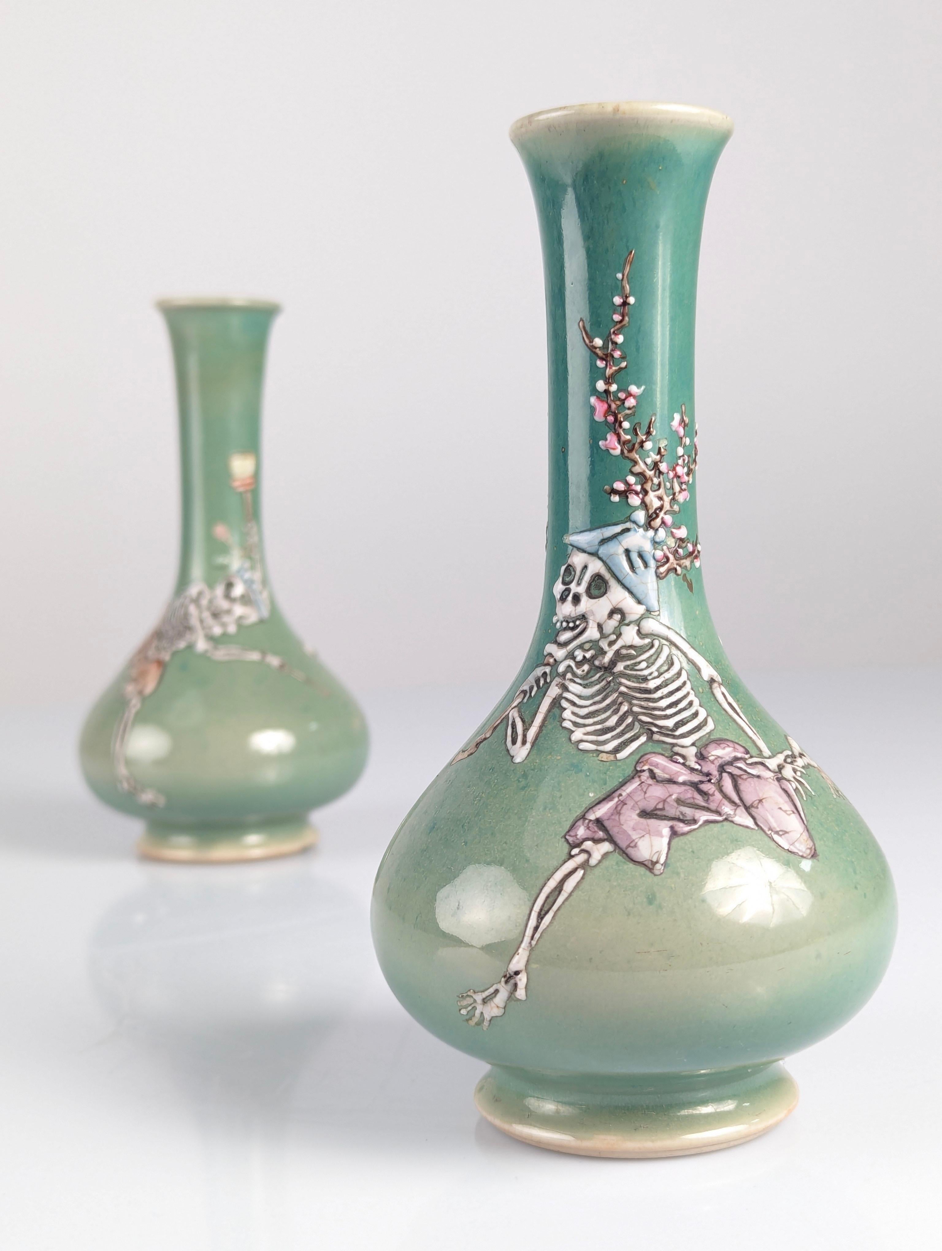 This pair of Japanese porcelain vases, in aqua green color, stand out for their unique and detailed skeleton relief theme. One vase features skeletons playing a mokugyo (Buddhist percussion gong), while the other shows skeletons carrying tree