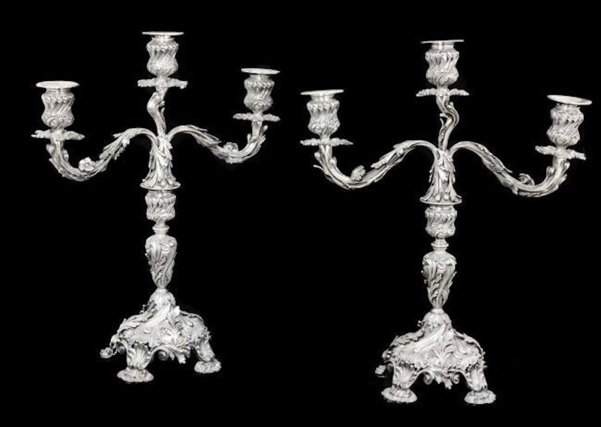 Pair of Portuguese silver three-light candelabra,
Lisbon, early 20th century,
in 18th century style, each on four shell and scroll feet, the domed base with cast scrolling foliage, rising to a baluster stem with foliage, the branches with