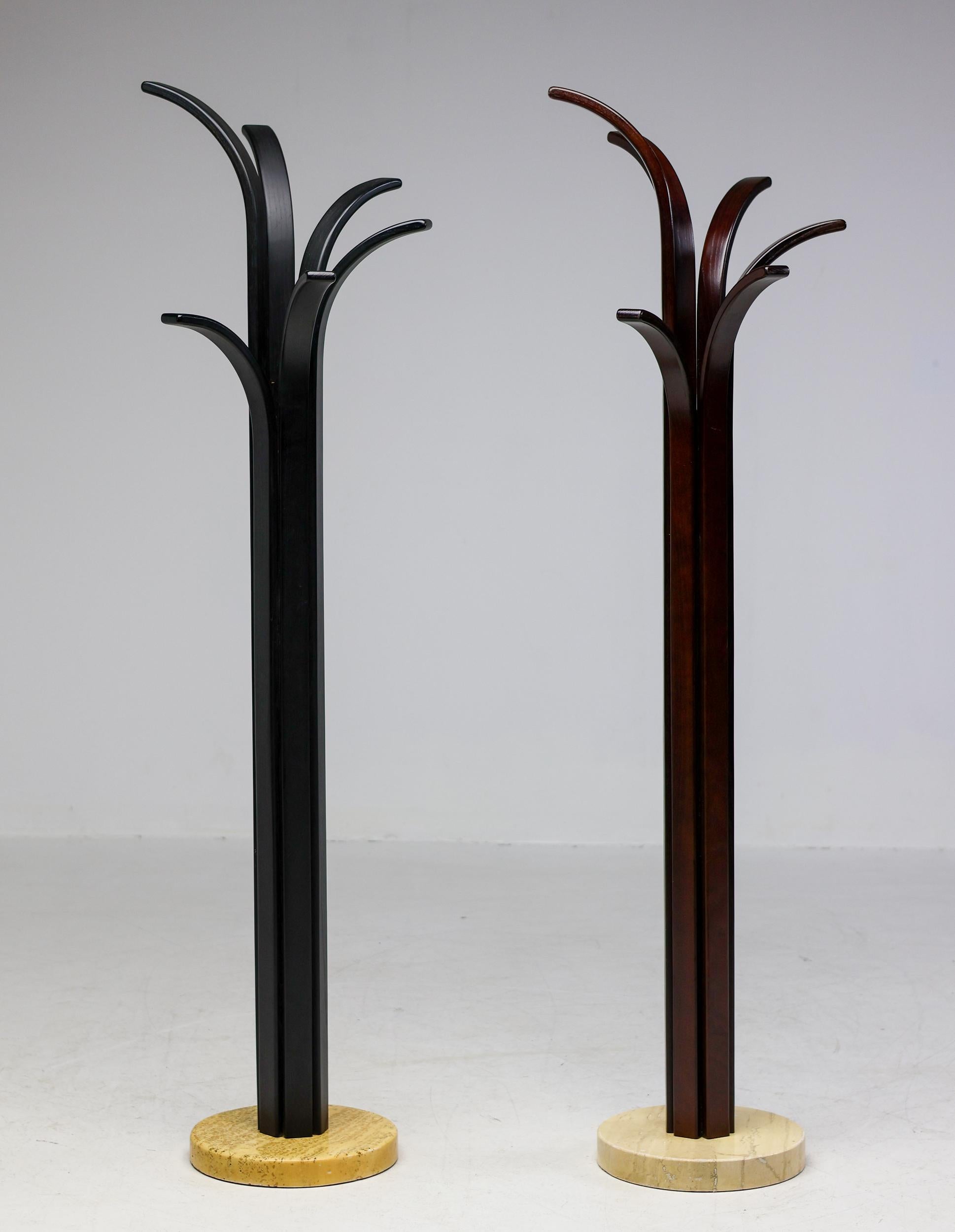 Pair of coat racks, signature example of Italian Post Modern design. 
Bases in travertine, one rack in black lacquered plywood slates, the second one in dark brown lacquered plywood slates. Manufactured in Italy in the 1980s.
The plywood uprights