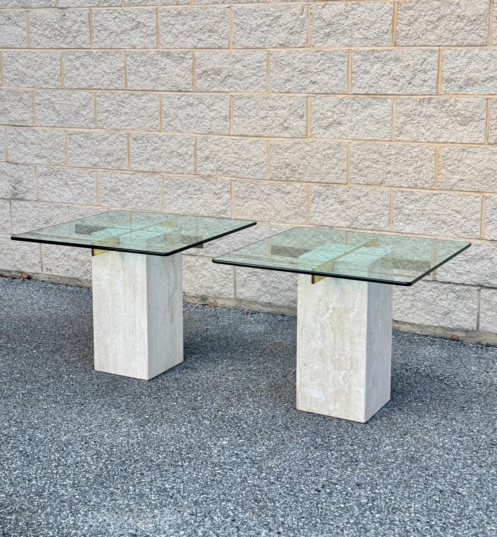 Paire de tables d'appoint postmodernes en travertin, avec des plateaux carrés en verre aux bords biseautés, soutenus par des bases rectangulaires en travertin. La base en travertin met en valeur sa texture de pierre naturelle et ses tons beiges,