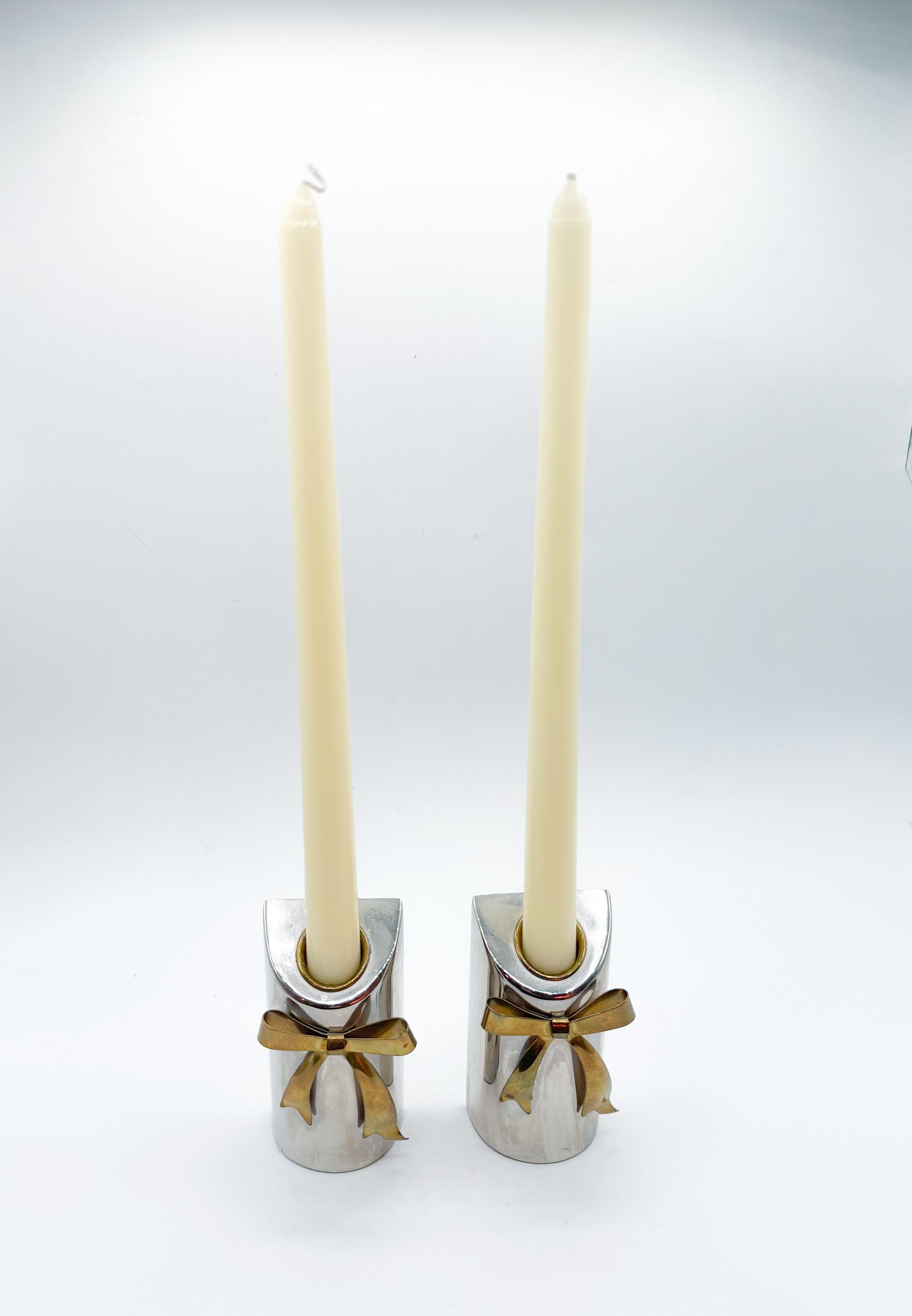 Whimsical yet refined, this sculptural pair of 1980s candle holders features a striking combination of polished silver-tone bodies and curved brass bows. With their mirrored symmetry and flat sides, they can be displayed together as a single