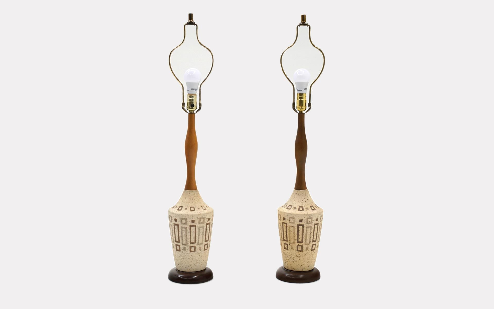 Pair of midcentury table lamps with ceramic bases and a sculptural walnut stem. Both lamps retain the original finials and shades.