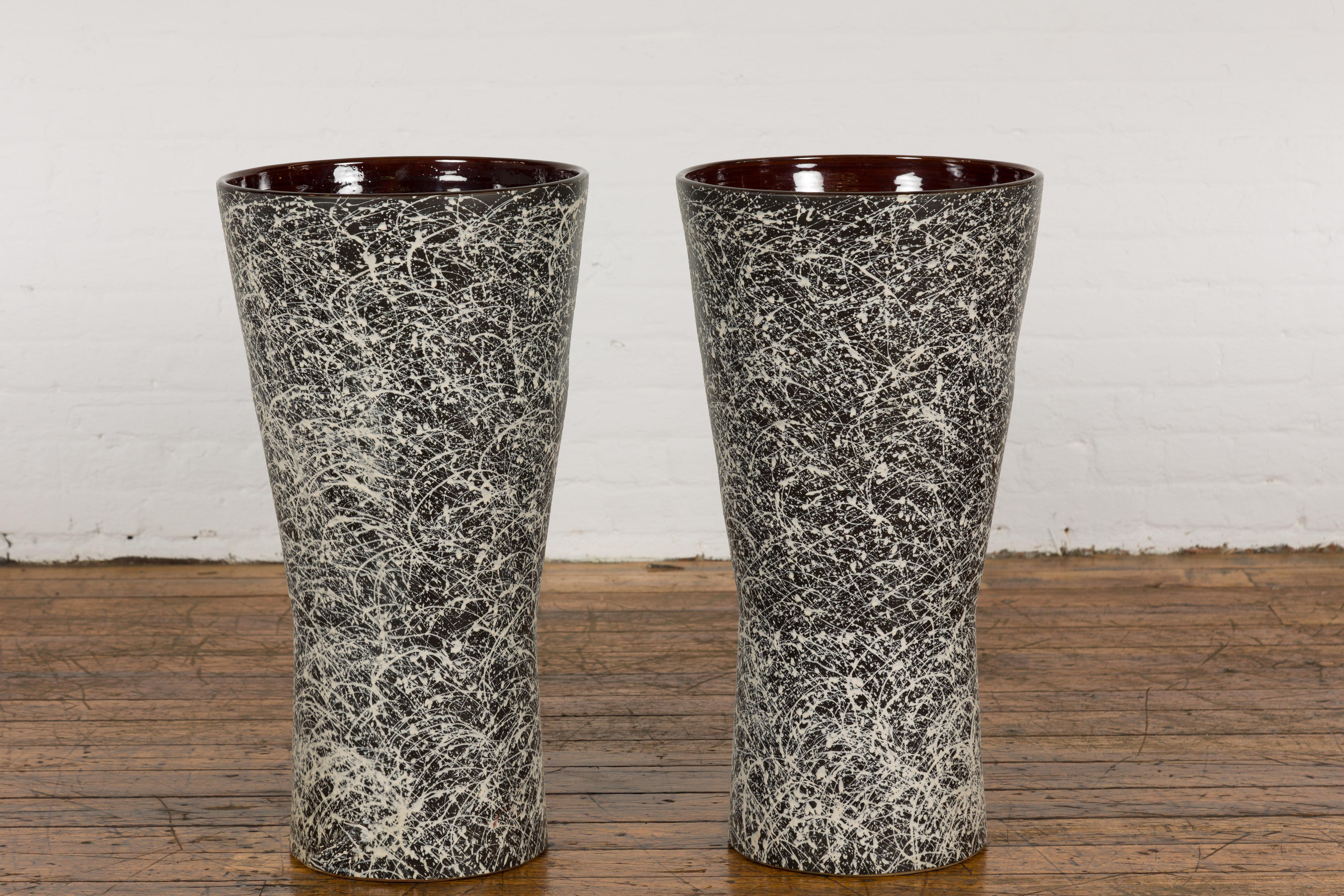 A pair of large artisan handcrafted Prem Collection vases with dark ground, energetic hand-painted white dripping décor, burgundy glazed interior and tapering lines. Experience the raw appeal of this striking pair of large artisan vases from the