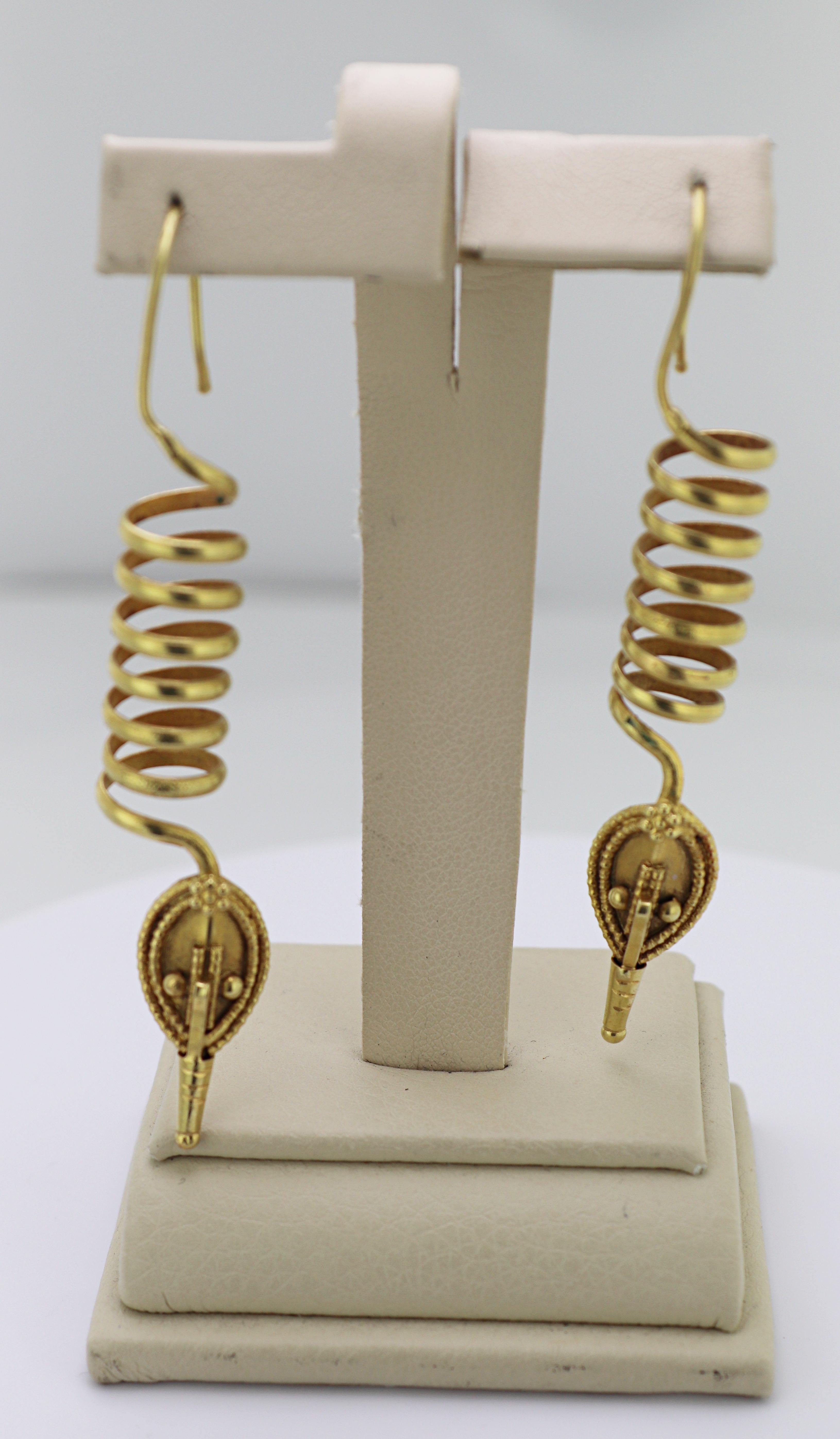 Each designed an 18k yellow gold long drop, featuring a 29 X 10 mm coil,
terminated by a primitive native mask motive with bead applique,
completed by a French wire hook, forming 3 inch long earrings, Total
Weight 14.7 grams.
