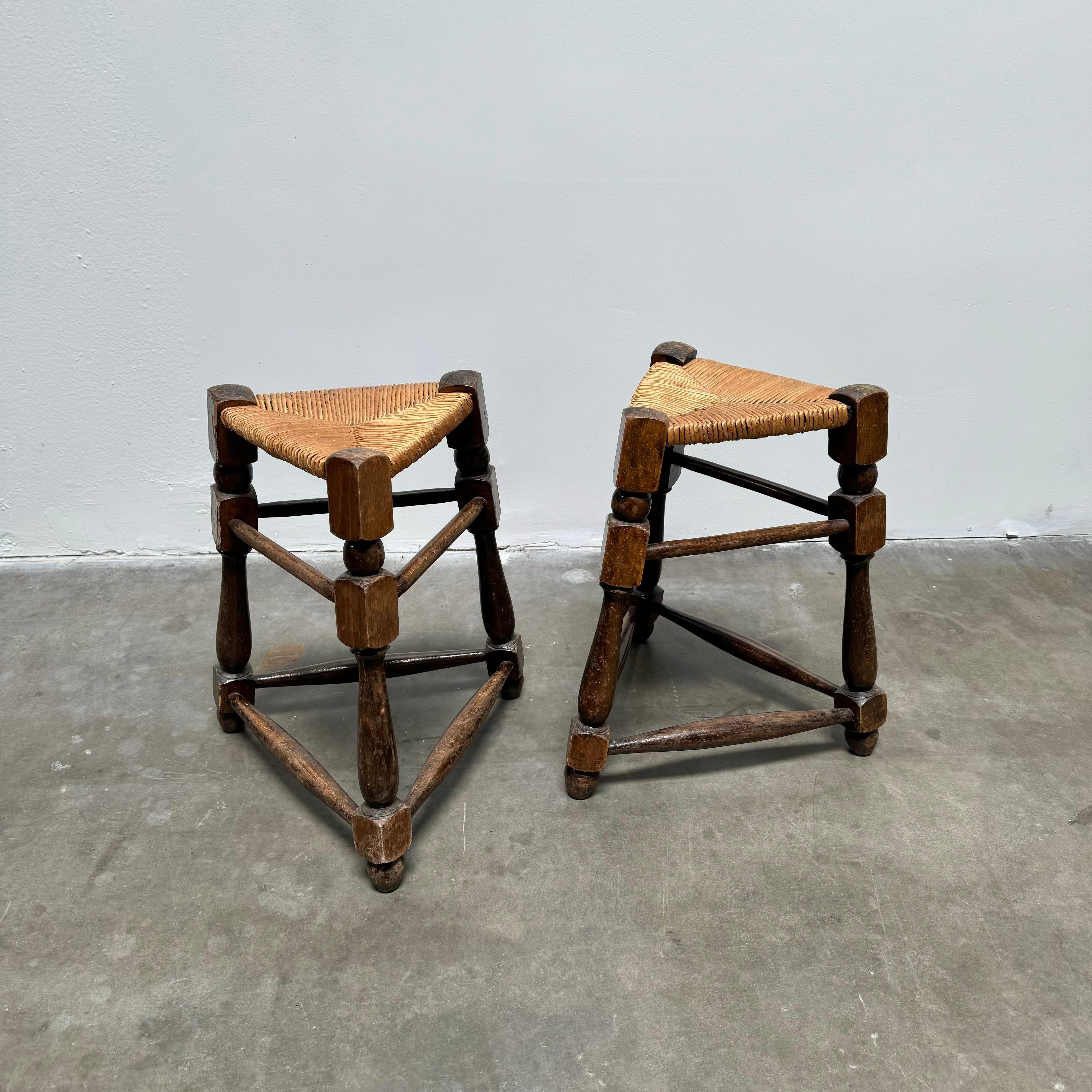 Paire de tabourets triangulaires de style provincial français du milieu du siècle, vers 1950.u2028Siège en jonc tissé à la main sur un cadre triangulaire en chêne tourné.

Un classique de la quintessence du design provincial français traditionnel.