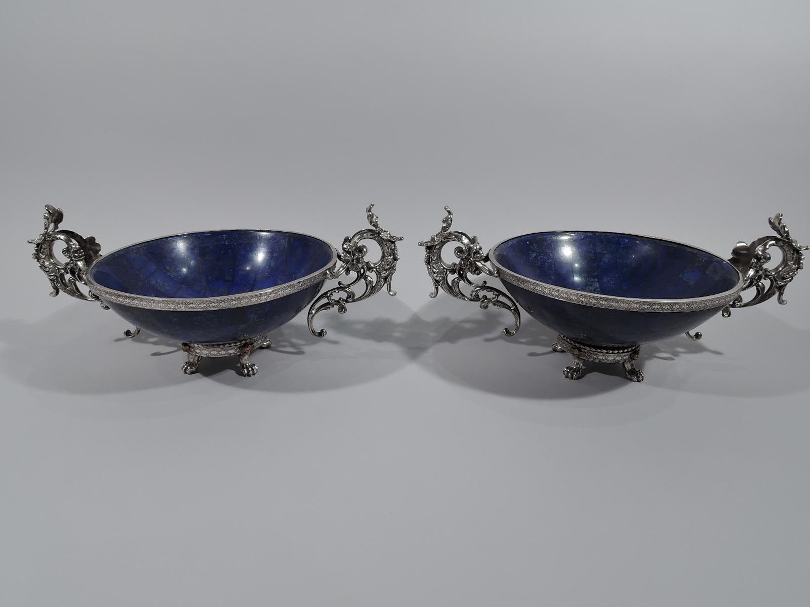 Pair of lapis lazuli bowls with 950 silver mounts. Made by Puiforcat in France, circa 1880. Each: Round tessellated bowl with silver rim collar and foot ring mounted to four paw supports. Elaborate open scroll side handles with leaves and flowers.