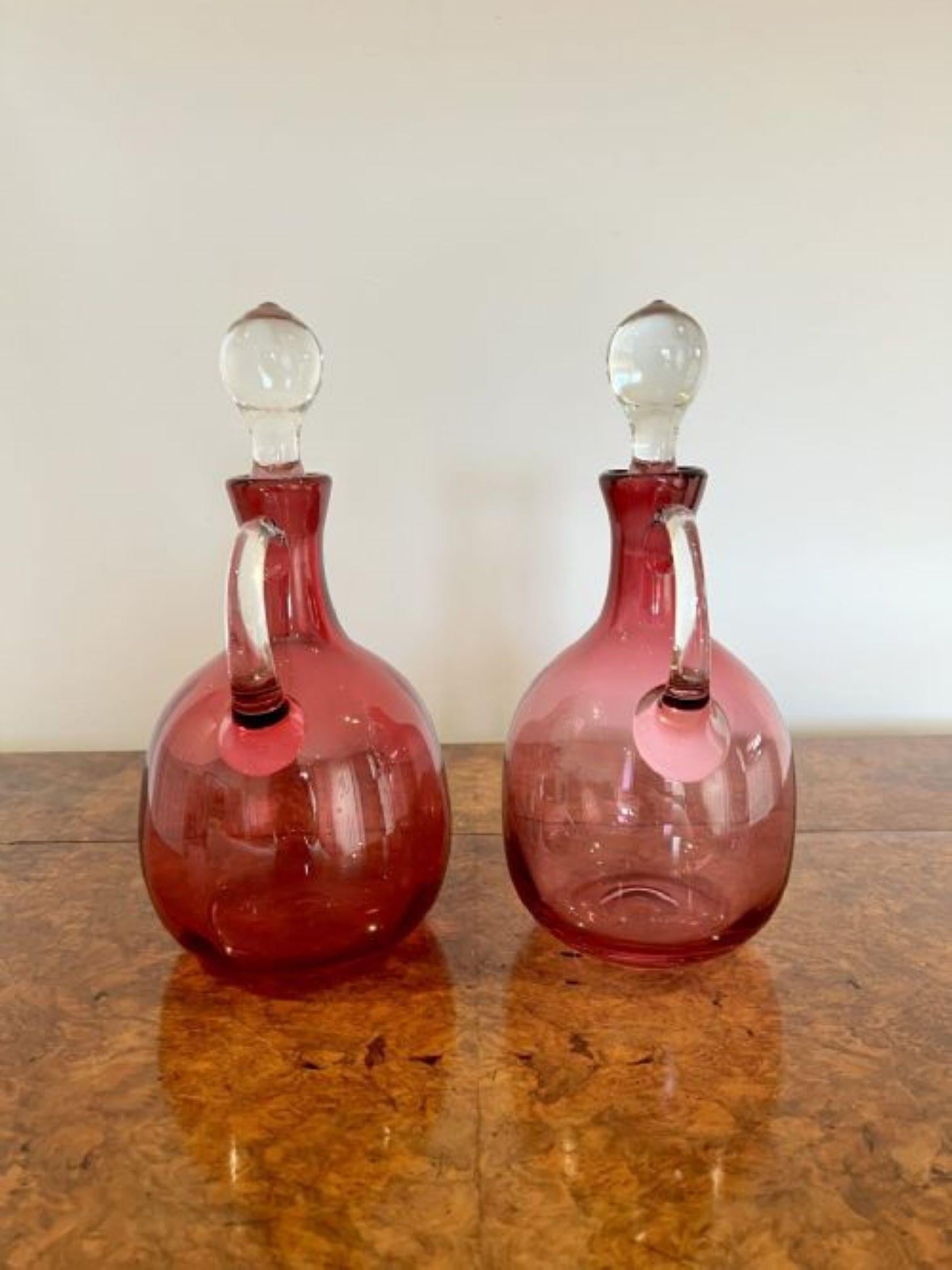 Pair of quality Antique Victorian Cranberry Glass Decanters with twelve cranberry glass wine glasses having a quality pair of antique Victorian cranberry glass decanters with a circular body and a shaped transparent glass handle to the back having