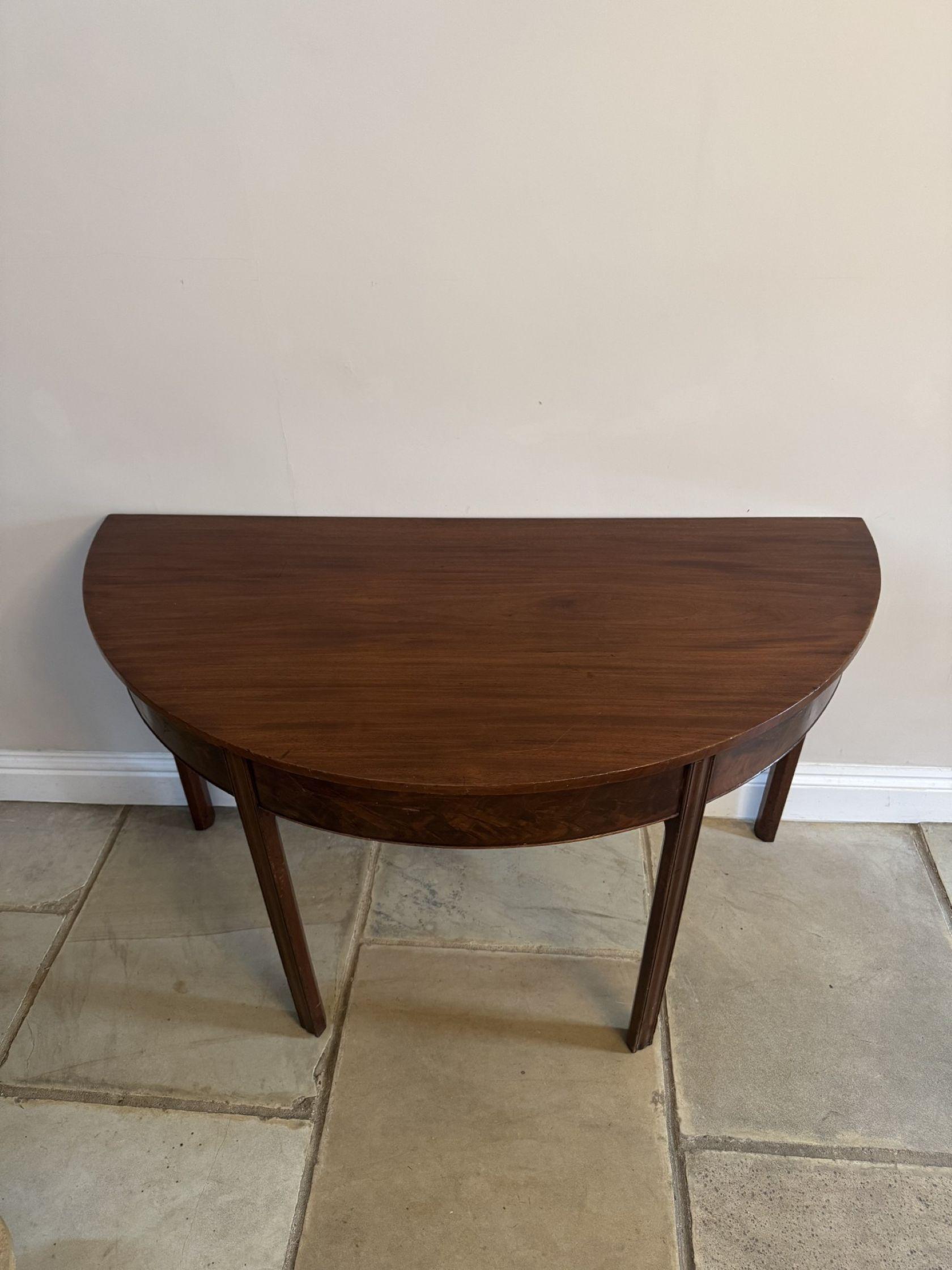 Pair of quality figured mahogany antique George III demi lune console tables, having a quality figured mahogany demi lune shaped top above a mahogany frieze, standing on four square shaped reeded tapering legs. 

D. 1800