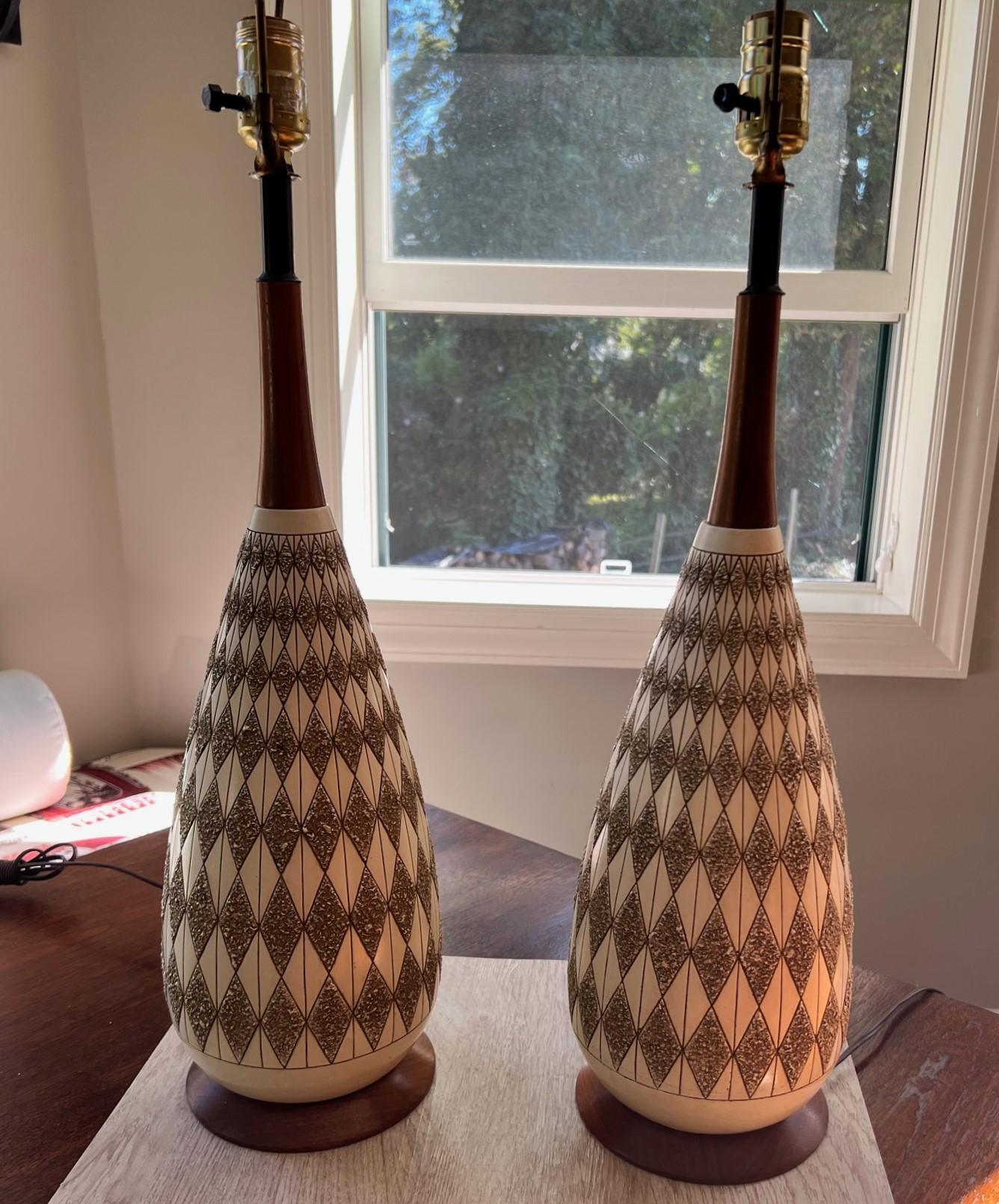A pair of Quartite Creative Corp. mid century modern table lamps in ceramic with teak accents. The lamp body is decorated in a crisp tapering ivory and textured brown argyle pattern. 

These lamps have a timeless appeal. Drum shades would take them