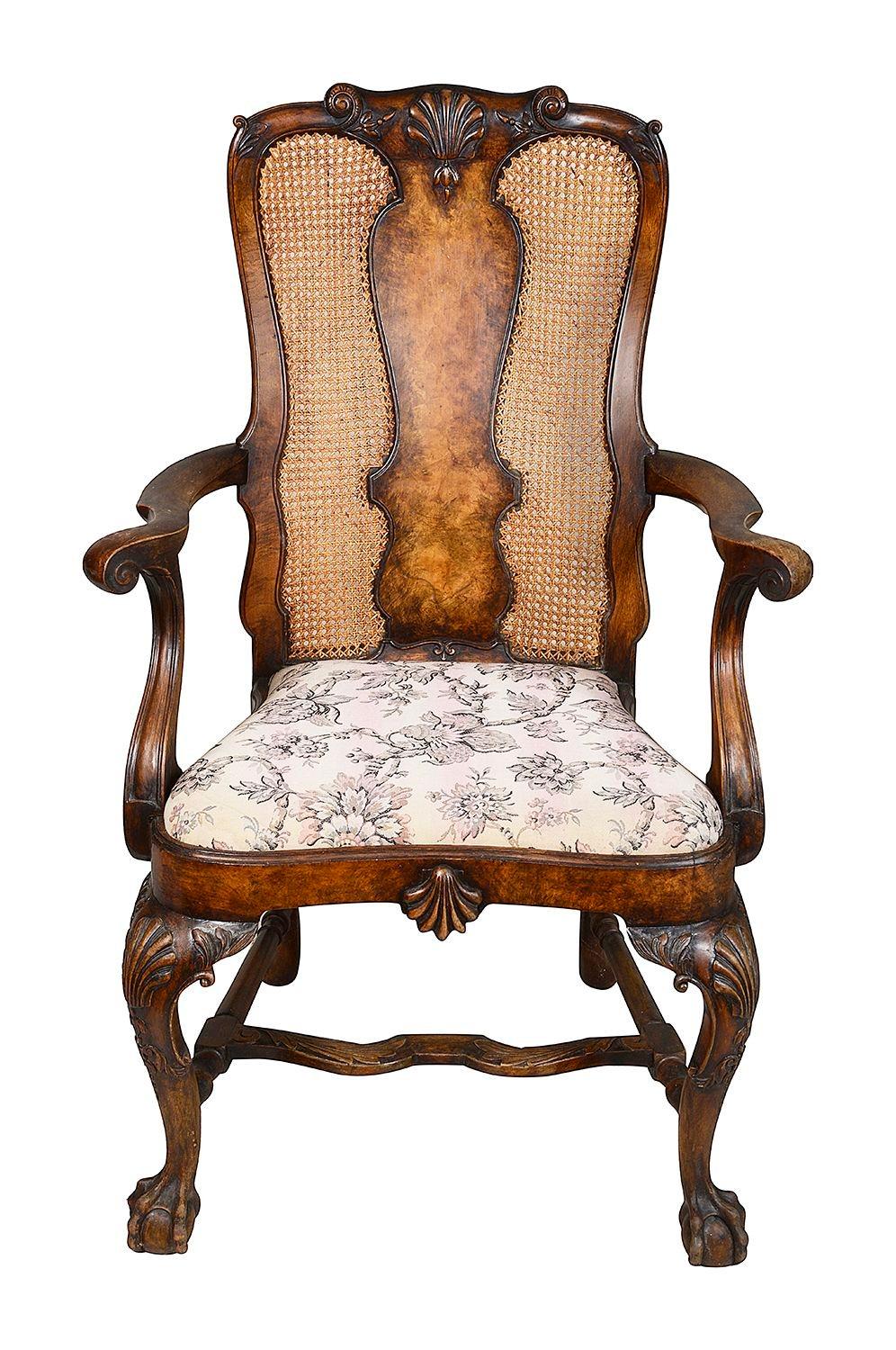 A pair of good quality burr Walnut, Queen Anne style arm chairs. Each with cane panels to the back rests, carved shell decoration, drop in upholstered seats, raised on cabriole legs, united by H stretchers and terminating in ball and claw
