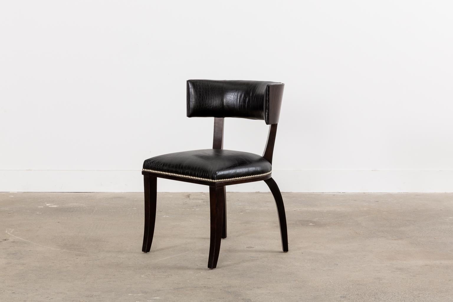 Gorgeous pair of neoclassical klismos style dining chairs designed by Ralph Lauren. The Clivedon dining chair features an ebonized hardwood frame with a gracefully curved, conforming backrest. The rest is veneered with a rich faux Macassar finish on
