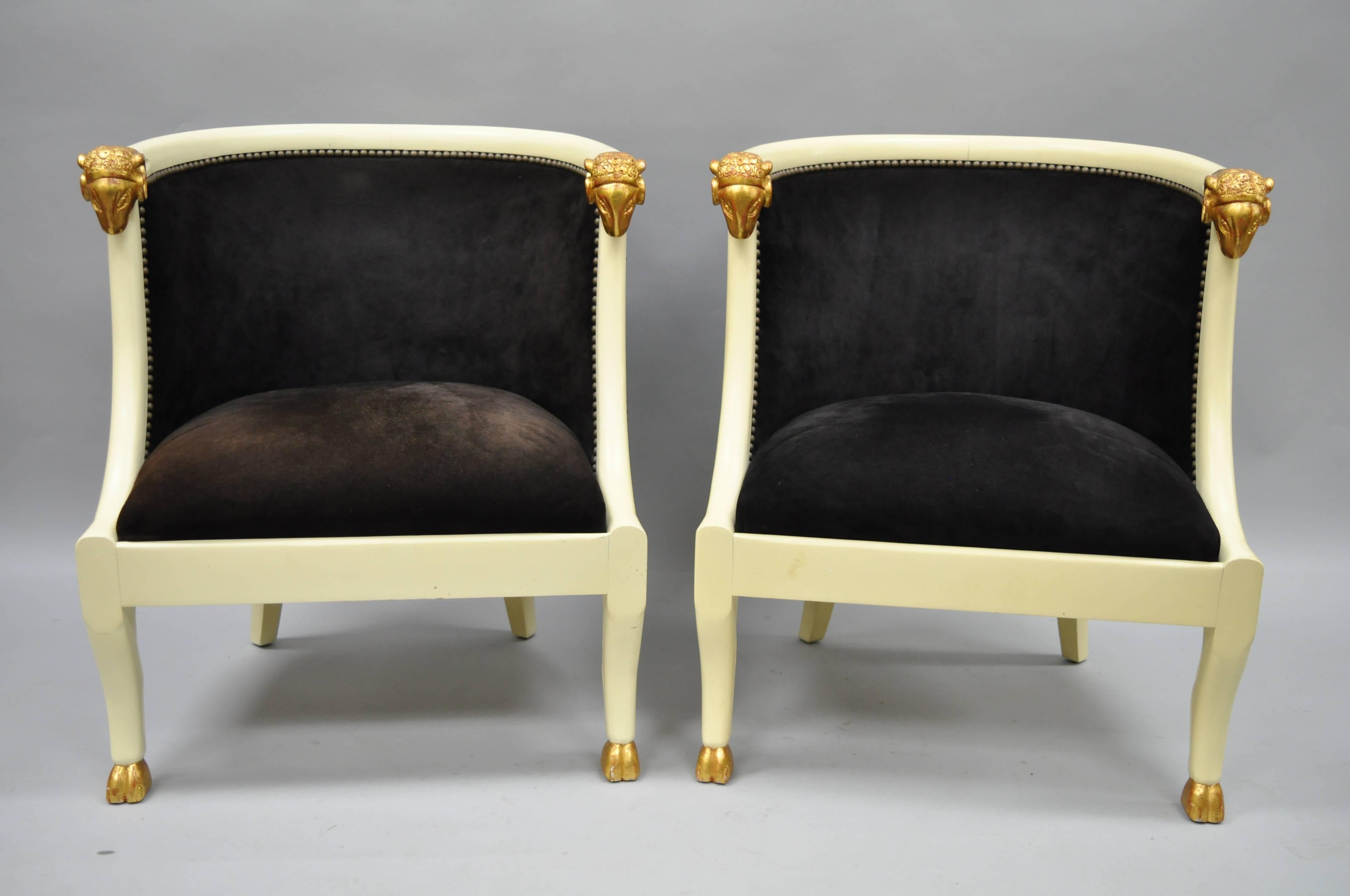 Impressive pair of ram's head Regency / neoclassical style barrel back chairs. Item features heavy solid carved wood frames, ram's head armrests, hoof feet, shapely barrel backs and blackish brown suede upholstery with nailhead trim. Chairs are