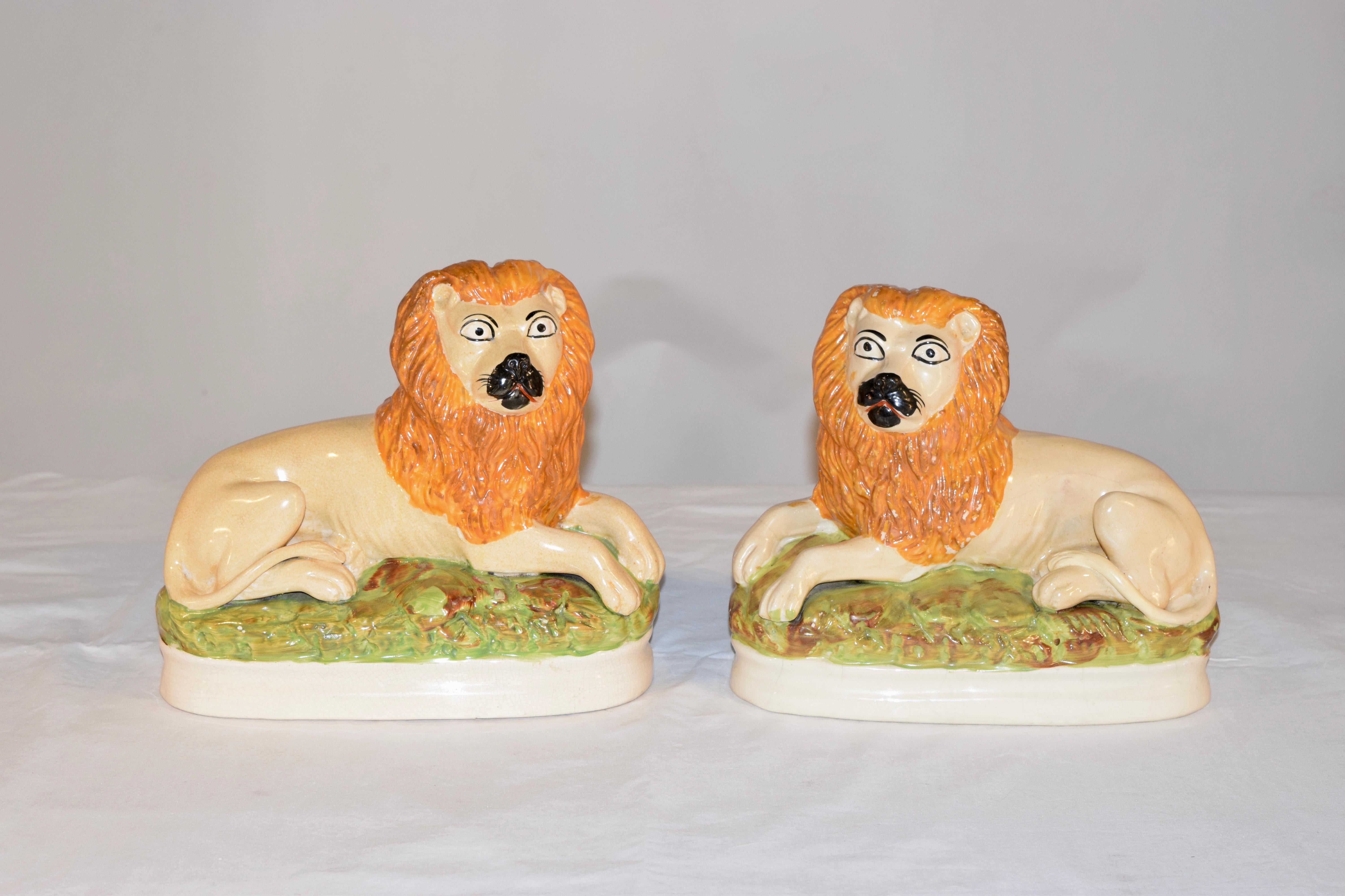 Pair of rare Staffordshire lion figures from England. The figures are lying lions on beds of grass, with their tails curling back around their bodies. The figures are richly hand painted in vibrant colors, which make them very unusual and