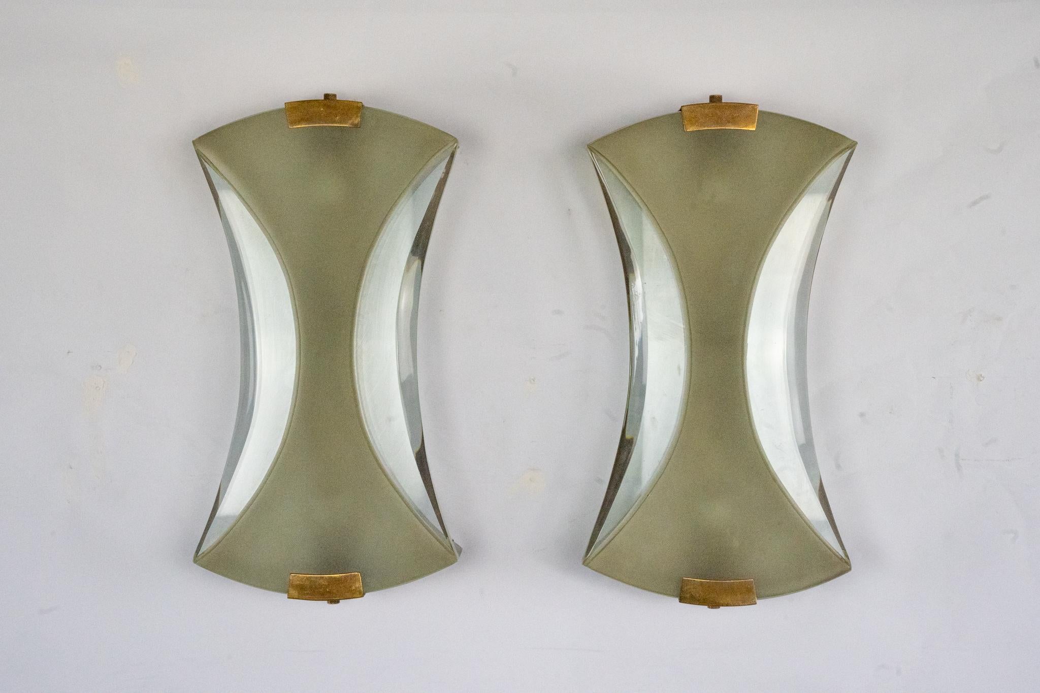 Este par de raras y elegantes lámparas de pared, diseñadas por Max Ingrand para Fontana Arte a principios de la década de 1960, presentan un importante cristal esmerilado con bordes biselados pulidos y detalles de latón. Cada candelabro presenta una