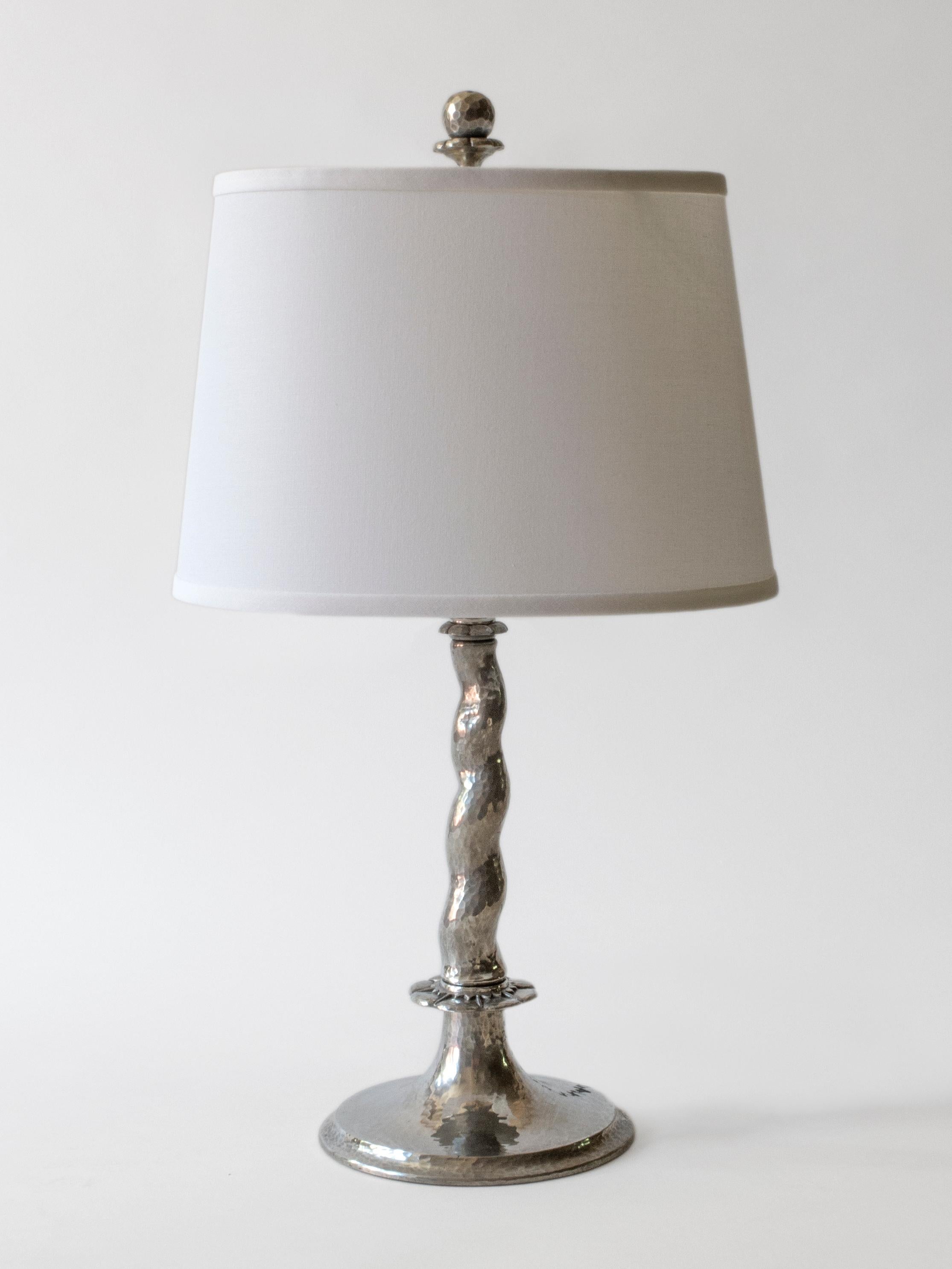 Each finial depicting a raised globe on a hourglass shaped blossom, surmounting a barley-twist stem, resting on a stylized rosette, terminating in a circular foot. 

Each lamp hammered throughout and with minor handmade differences. The overall