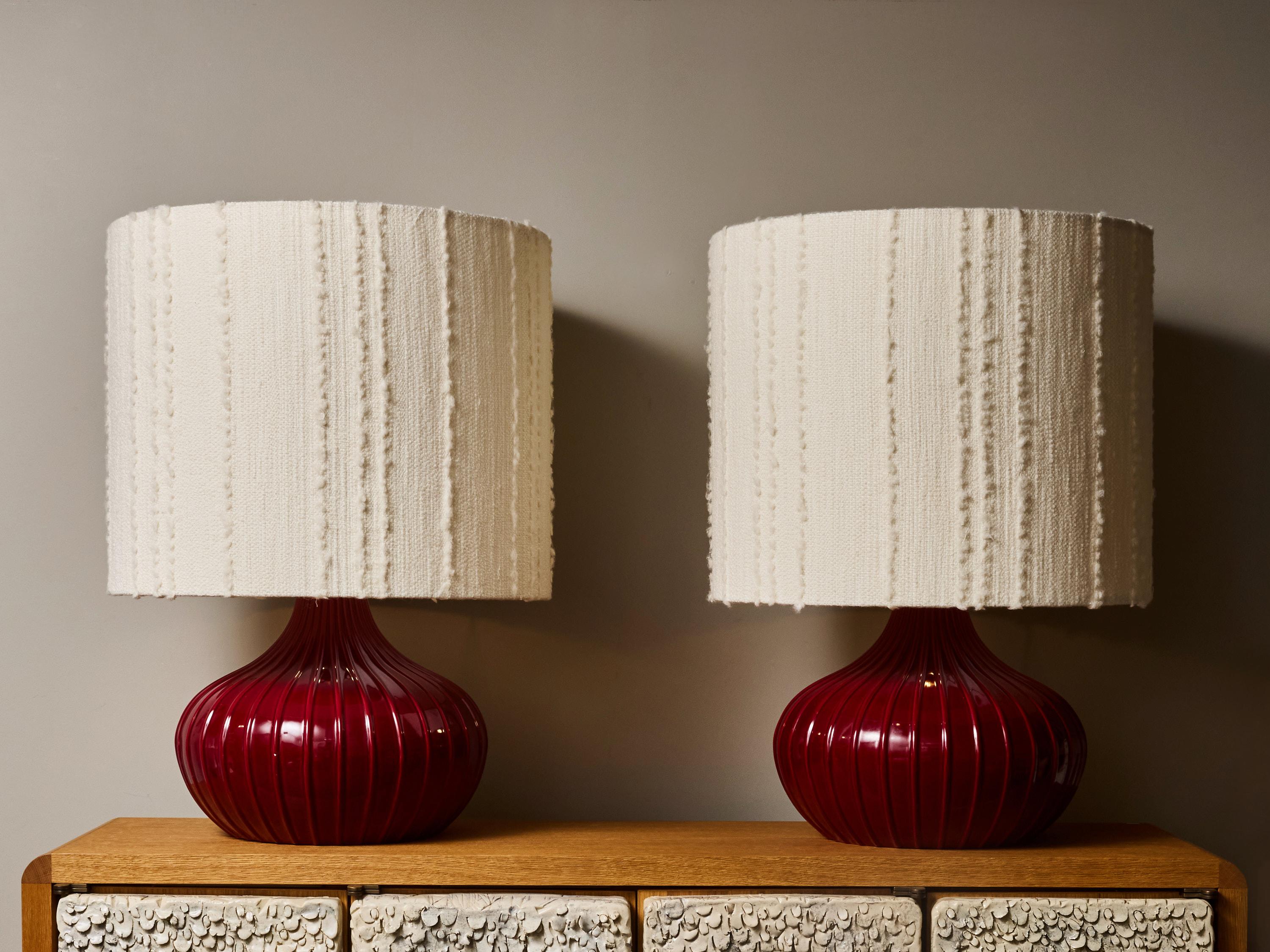 This elegant pair of Italian table lamps from the 1980s features sculptural ceramic forms distinguished by their rich, deep red glaze and beautifully ribbed silhouettes. Each lamp showcases a harmonious blend of soft curves and vertical fluting,