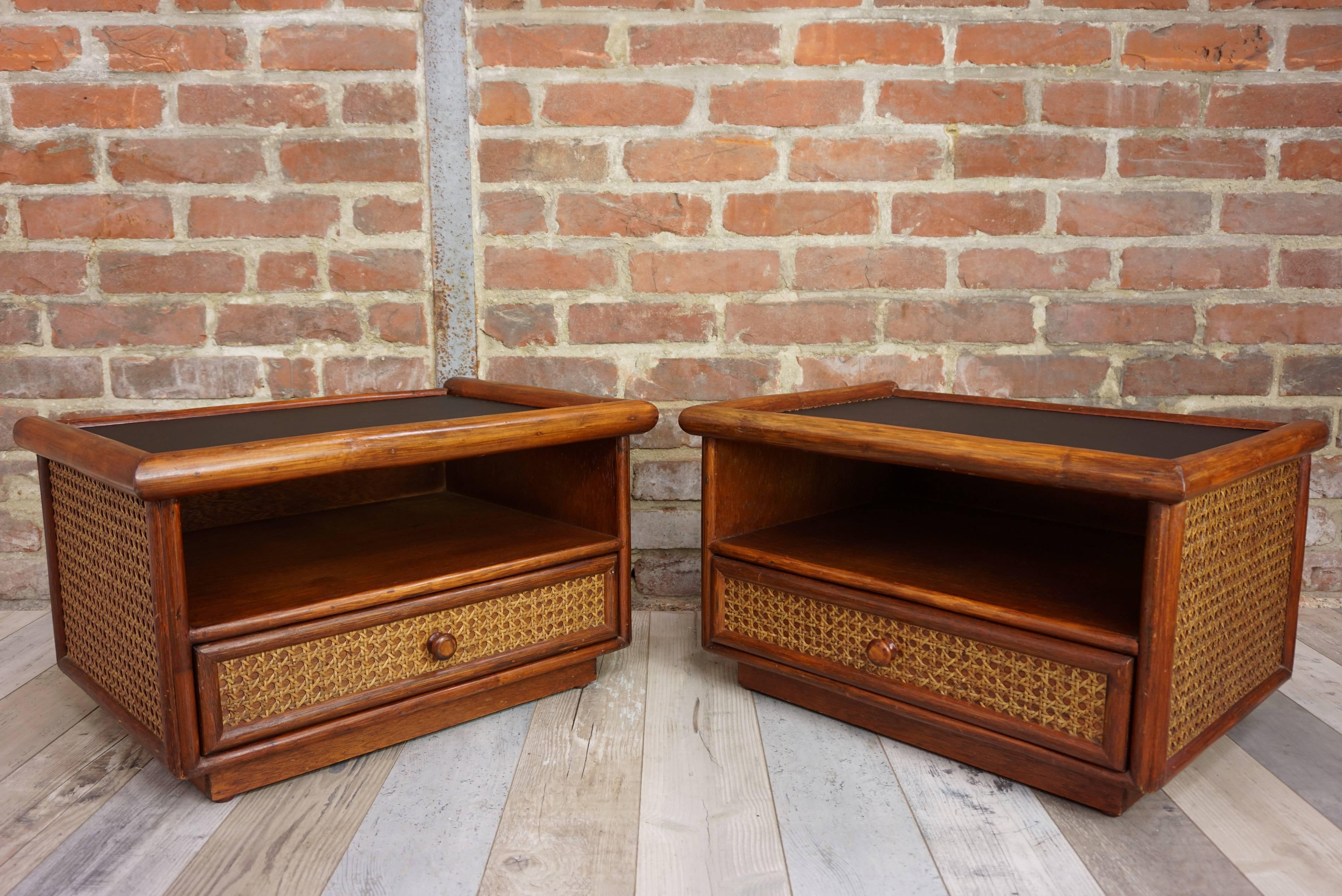 Pair of bedside tables from the 1960s-1970s composed of a wooden and rattan structure, dressed with cane black faux - leather for the tray. All in beautiful state of conservation!