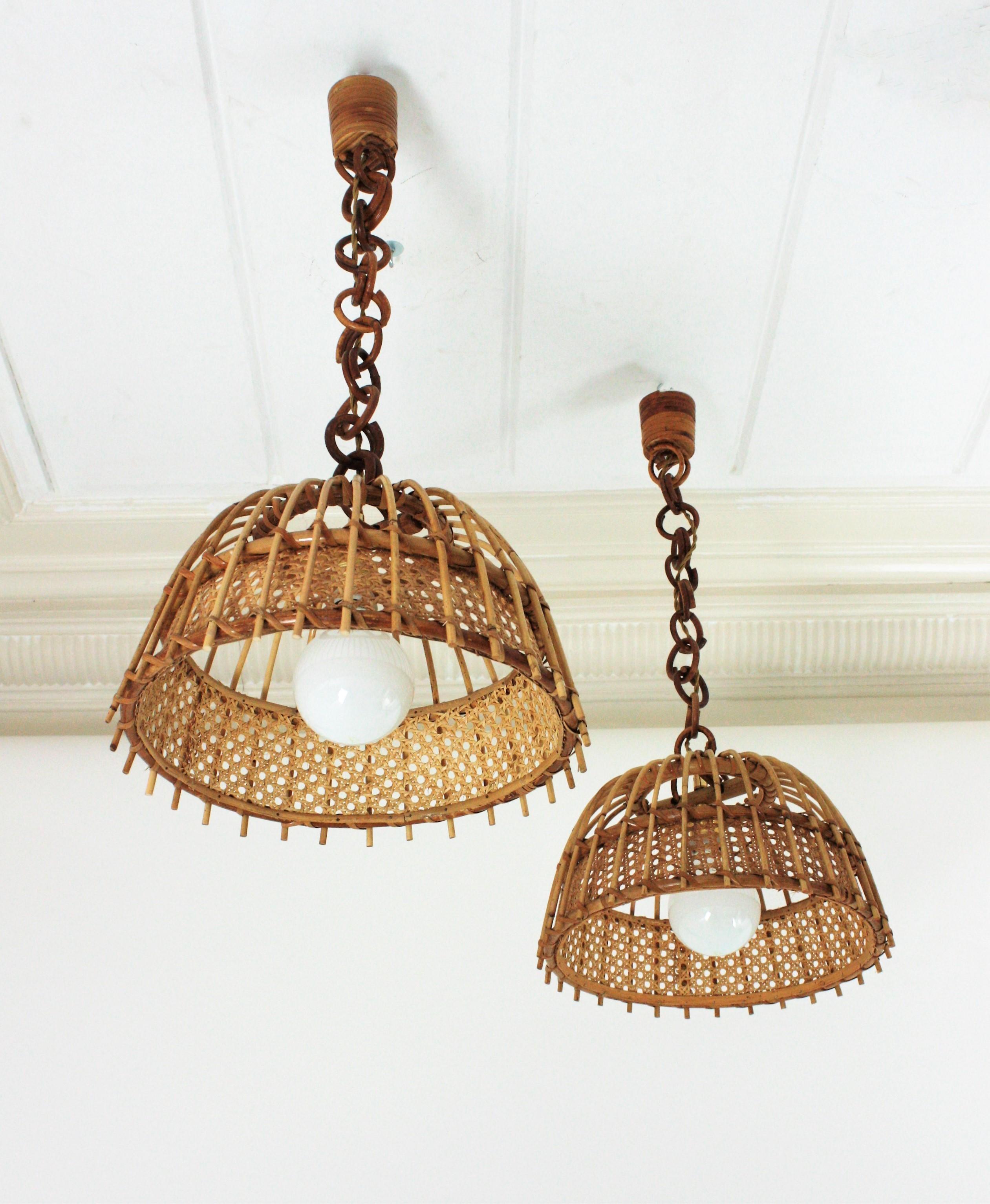 Spanish modernist rattan and wicker weave suspension lamps with bell shaped shades, Spain, 1960s.
These pendats feature a rattan bell shaped shade with vertical canes accented a woven wicker wire horizontal band.
They hang from chains with round