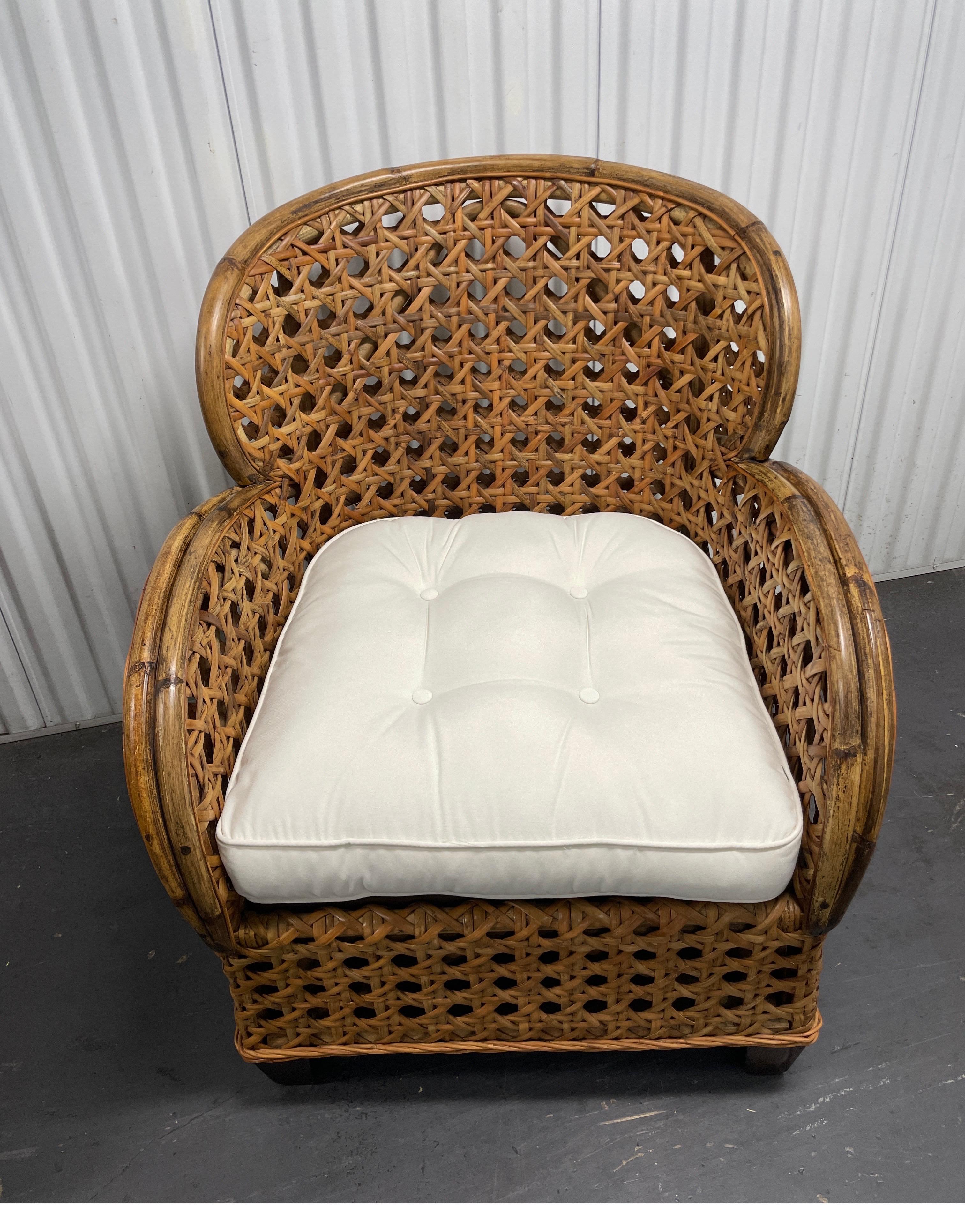 Vintage pair of French inspired rattan and cane arm / club chairs with white seat cushion in an art deco style.