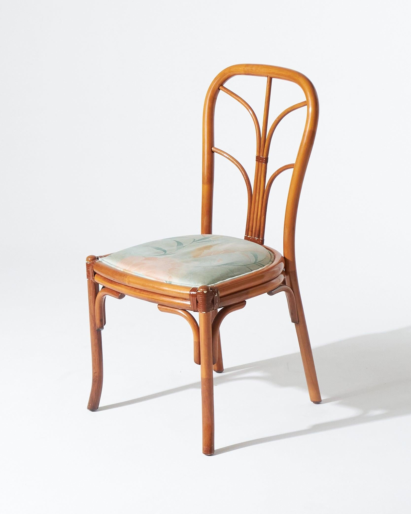 Pareja de sillas de ratán curvado estilo bambú. El asiento está tapizado en una elegante tela floral en suaves tonos verde mar y rosa rubor. Se aprecia un ligero desgaste de la madera, que no le resta encanto natural.