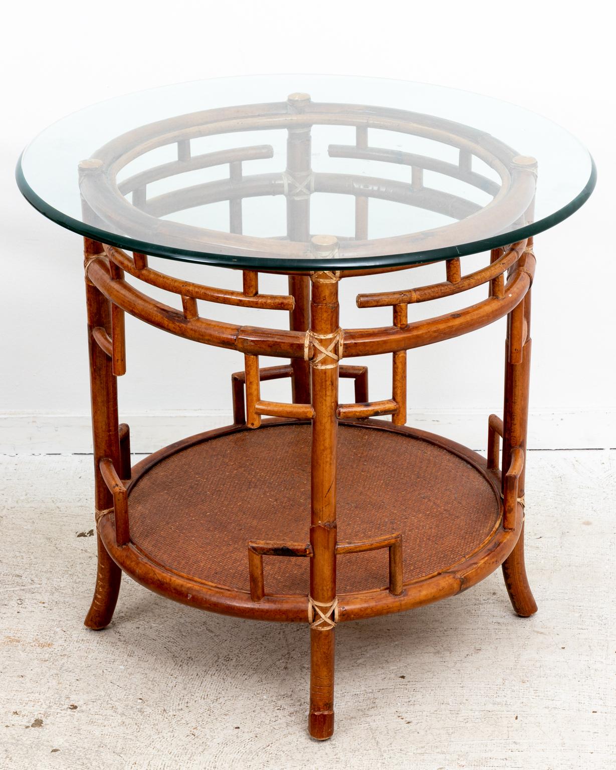 Circa 1970s pair of rattan Chippendale style round tables with glass tops, bottom shelf, and fretwork sides. Please note of wear consistent with age.