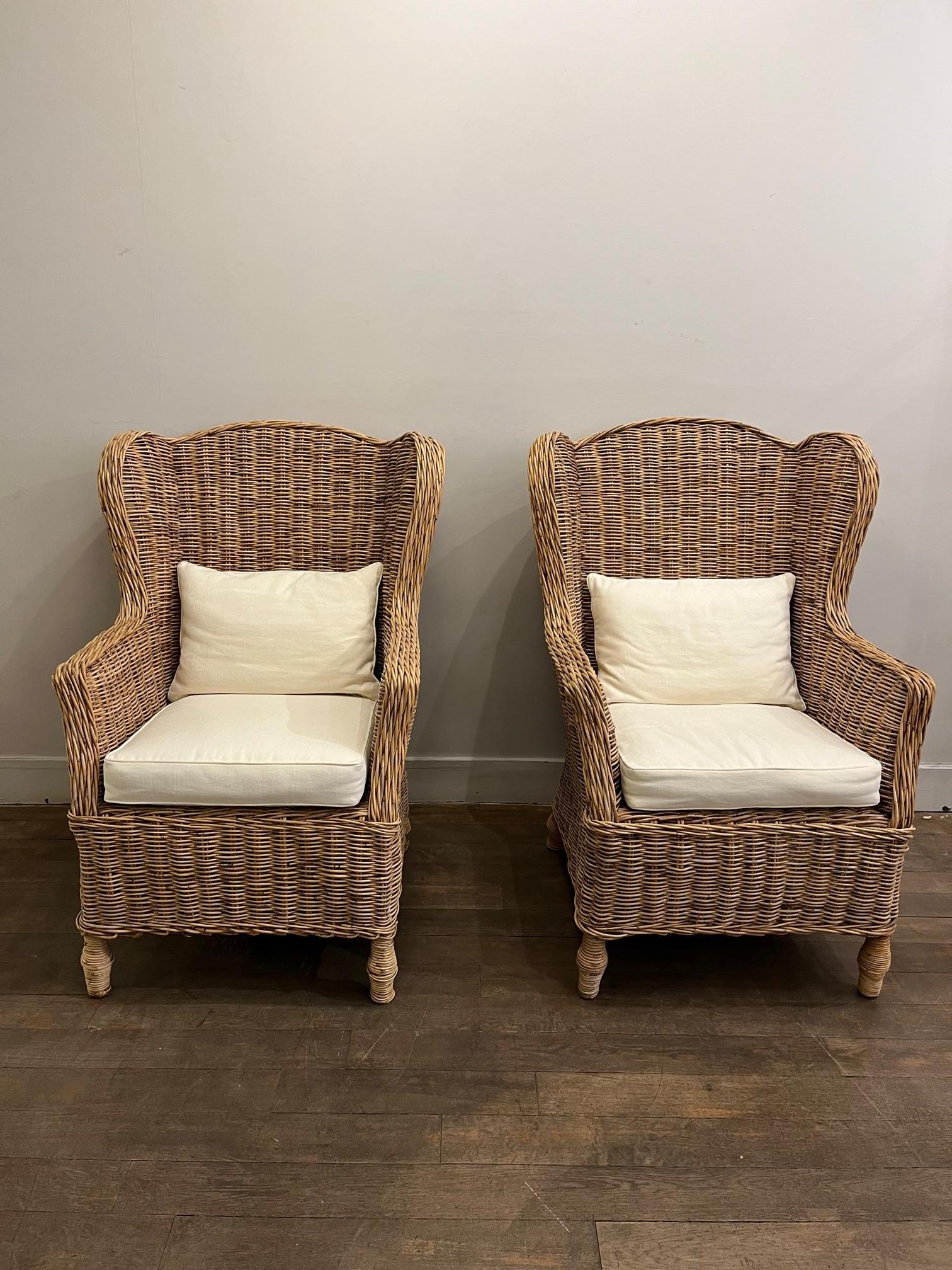 Pair of rattan high back wing chairs. 
White cotton cushion ( newly upholster ) 
France 1970

Dimensions, Measures: 

Hauteur / Height : 107 cm / 42.51 inch
Hauteur d’assise / Seating height : 50 cm / 19.68 inch 
Largeur / Width : 79 cm /