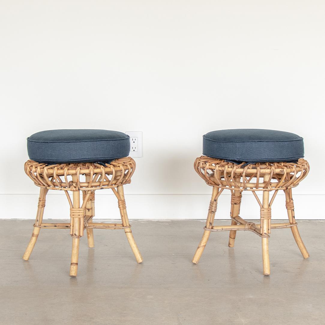 Beautiful pair of rattan stools in the style of Franco Albini from the 1960's. Curved rattan seats with four legs and wrapped rattan detailing. Newly upholstered circular seat cushions in navy blue linen.