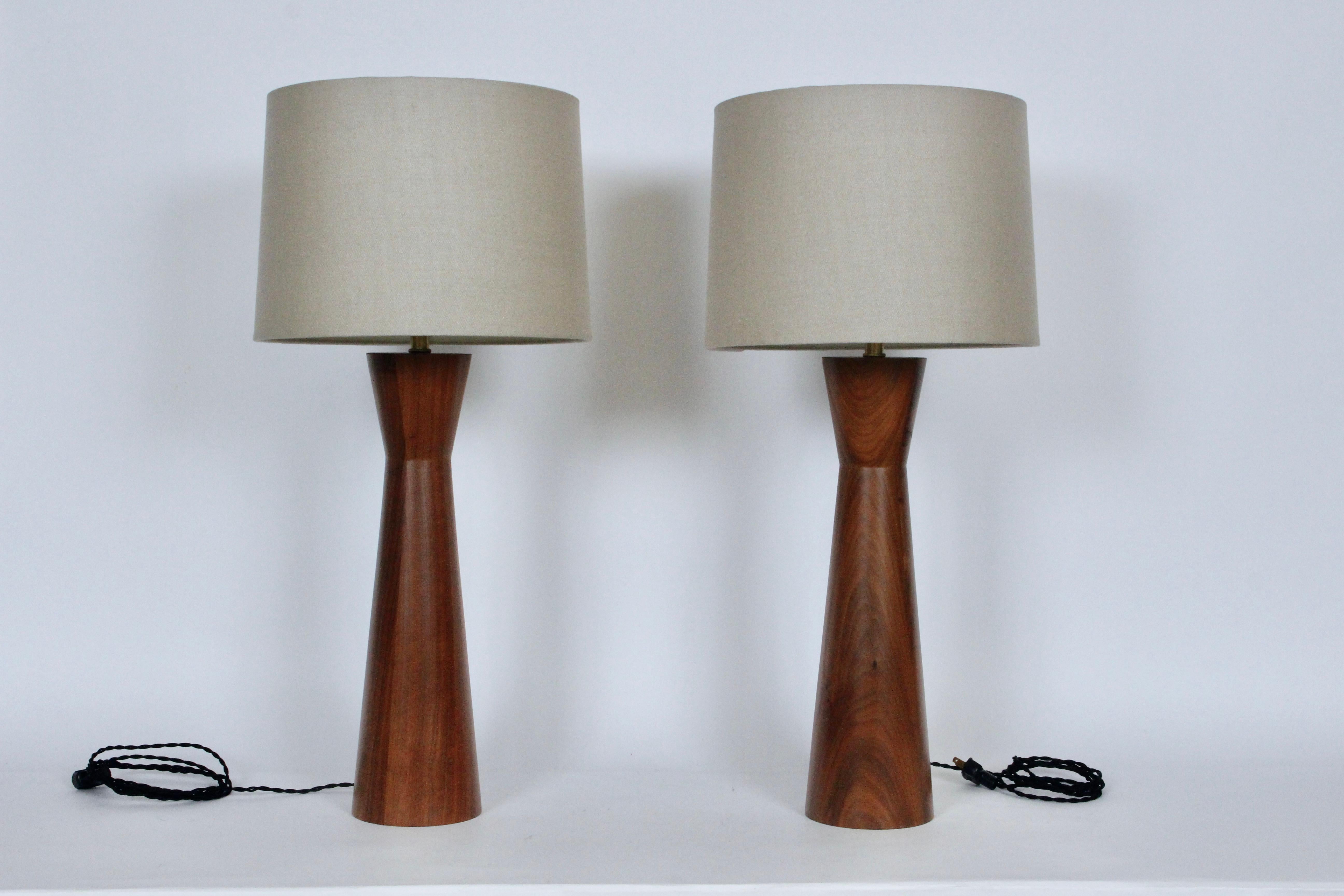 Pair of California Modern Raymond Pfennig for Zina Lamp Company walnut bedside table lamps, 1960s. Featuring a sculpted hourglass form in stacked walnut. Measure: 22H to top of socket, 18H to top of walnut. Lamp shades shown for display only and not