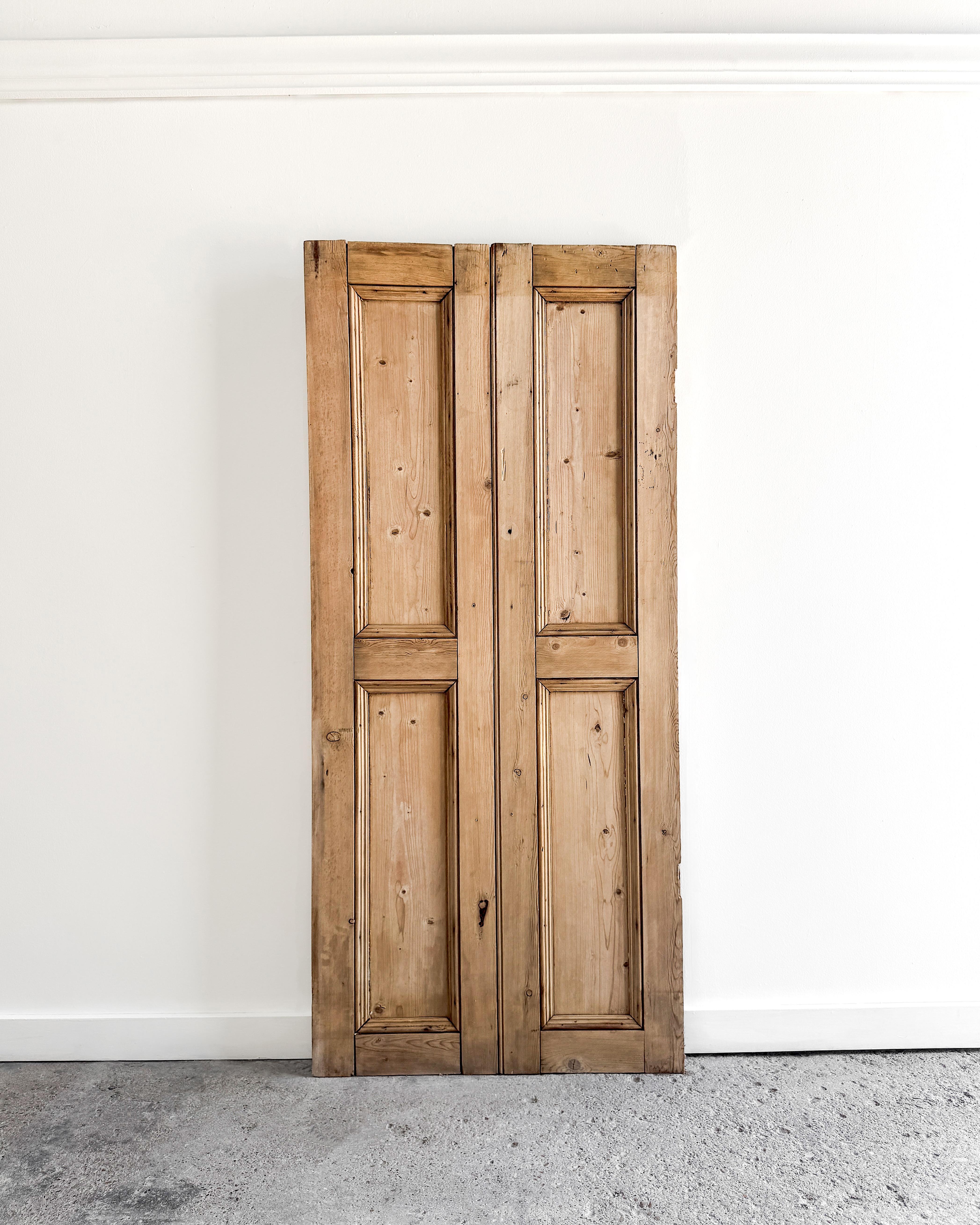 A reclaimed pair of 2-panel cupboard doors from 19th-century England, crafted from raw pine with classic beveled trim. Whether used to enclose a built-in cabinet or mounted as architectural wall accents, they bring warmth, age, and a quiet sense of