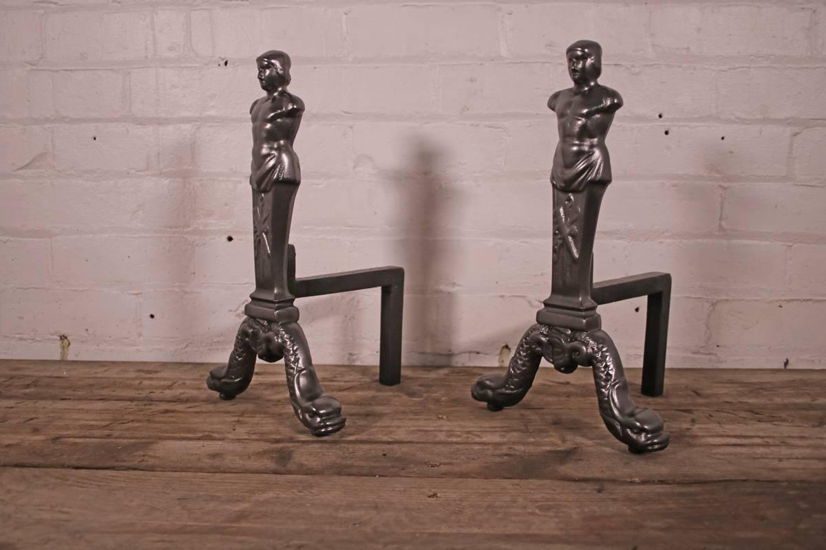 Pair of reclaimed cast iron male-form neoclassical andirons. A male head and torso sits above the stem decorated with a torch and quiver, the whole supported on splayed feet in the in the form of a pair of dolphins, mid-late 19th century. Finished