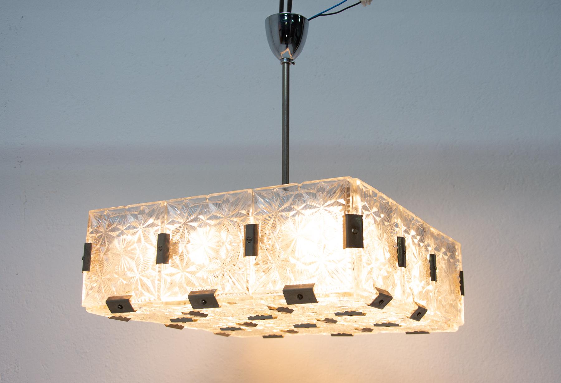 This rectangular crystal glass and chromed pendant lamp was made in the former Czechoslovakia in the 1970s.  It was made by Kamenický Šenov company. Made of glass and metal. It´s composed of thick textured patterned square cut fetal piece with