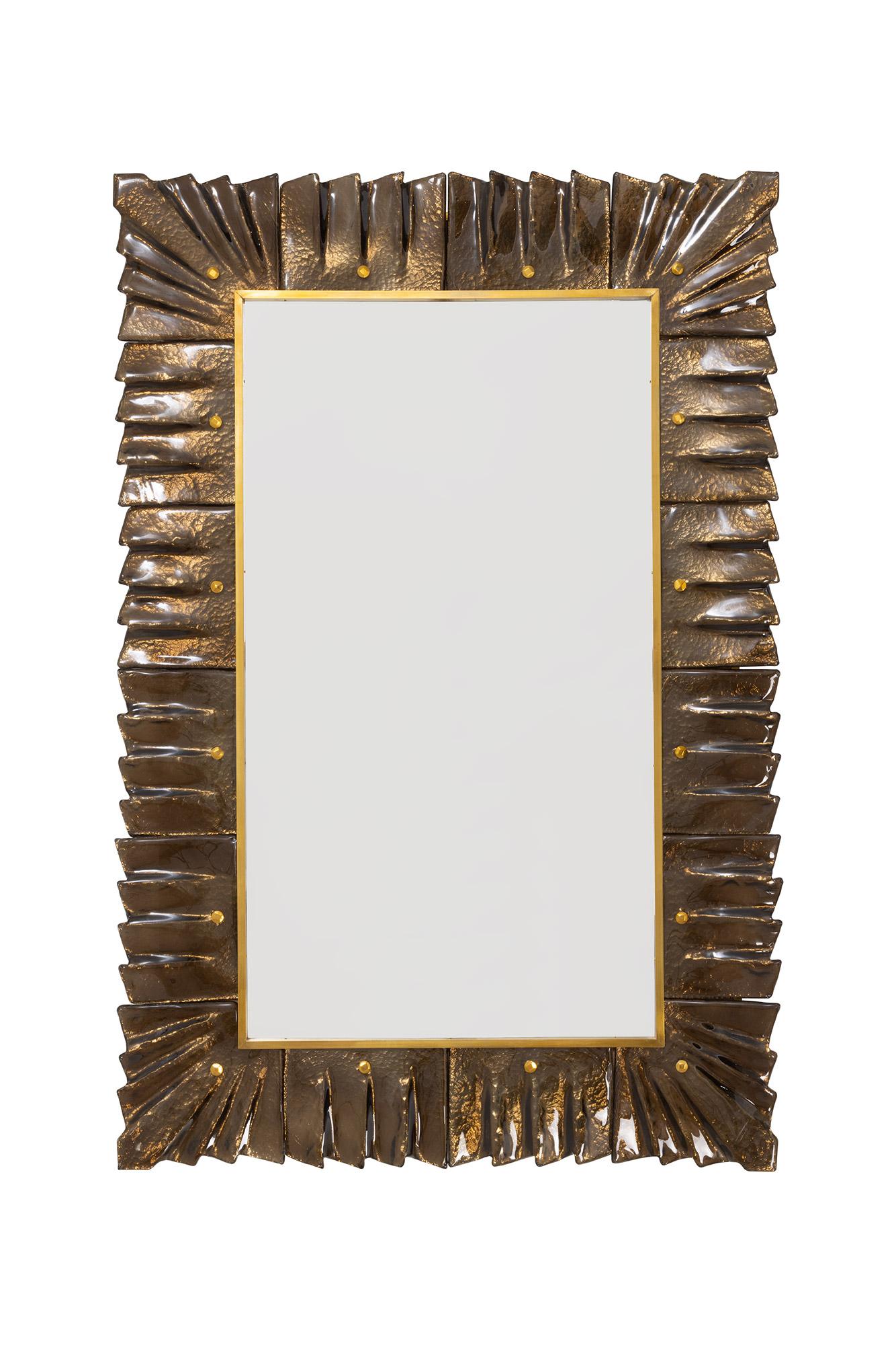 Paire de miroirs encadrés en verre ambre/bronze de Murano, en stock.
Plaque de miroir rectangulaire entourée de carreaux de verre ondulés de couleur ambre/bronze retenus par des cabochons en laiton. 
Fabriqué à la main par une équipe d'artisans à