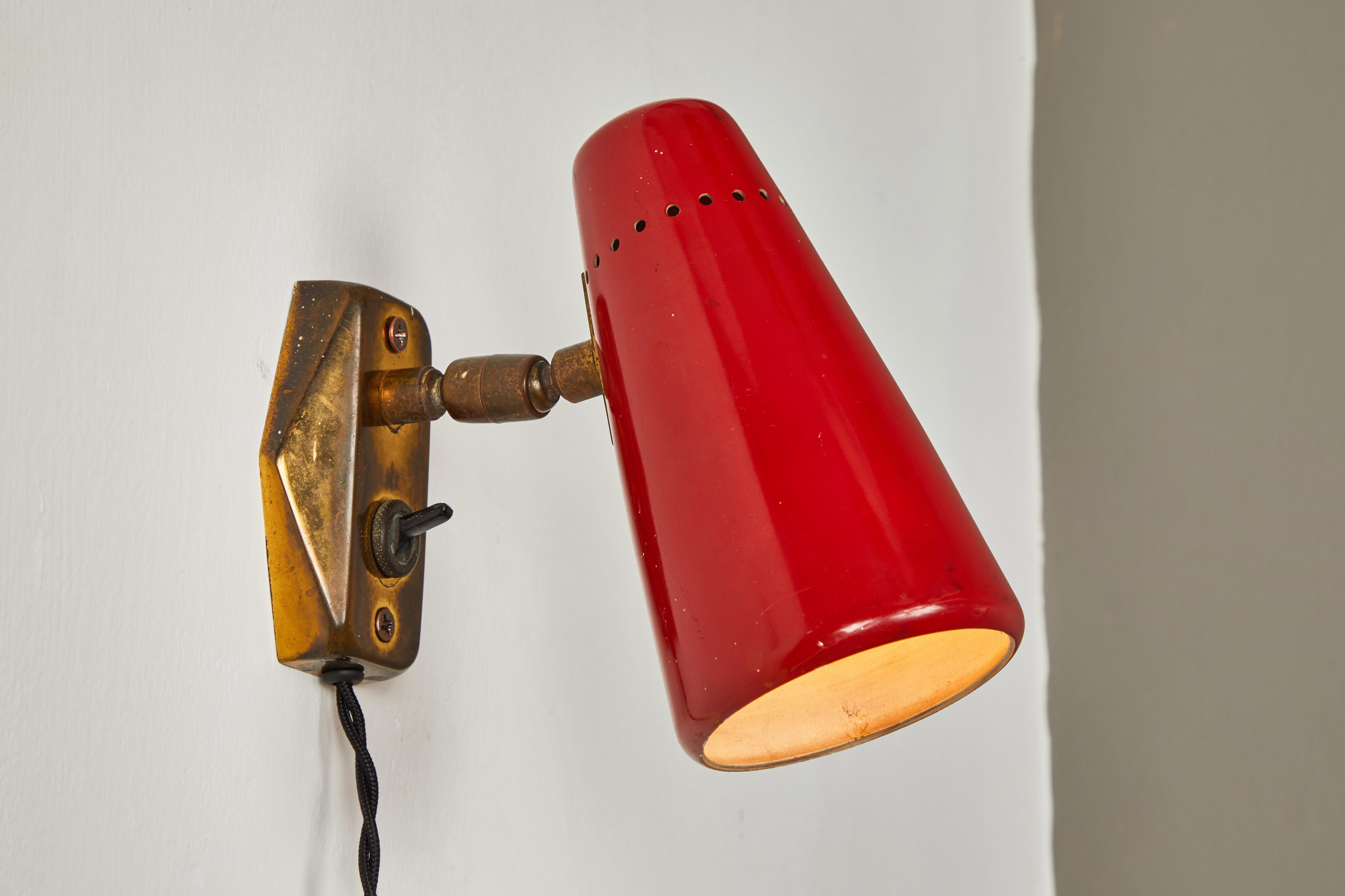 Pair of red 1950s Stilnovo sconces. A quintessentially 1950s Italian design executed in red painted metal with original Italian backplates, black cloth cord and US period styled wall plug. Shades can be rotated freely on a brass ball joint. Retains