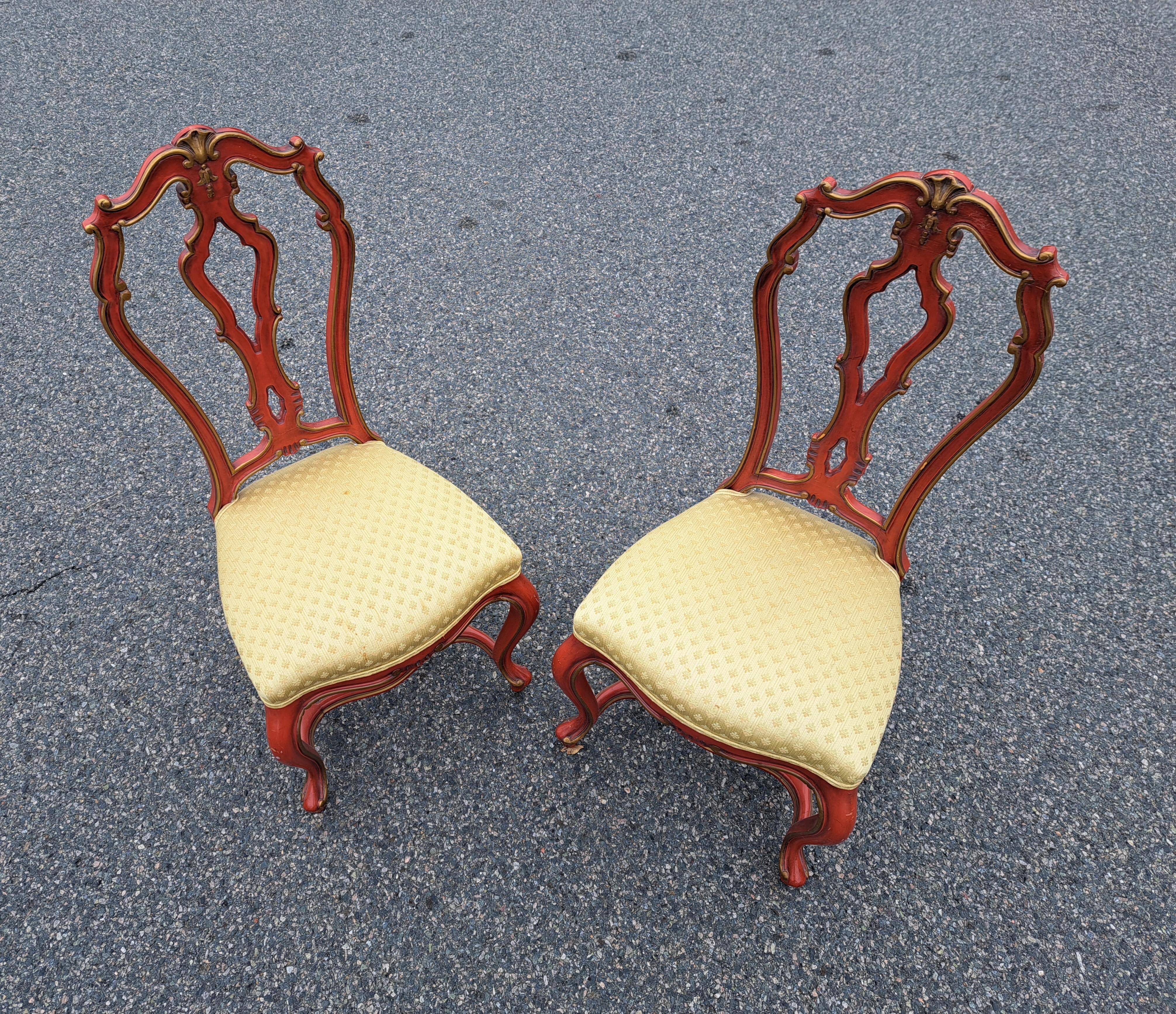 Coppia di sedie da pranzo rosse in stile Hollywood Regency con accenti dorati, schienali intagliati e gambe ricurve.