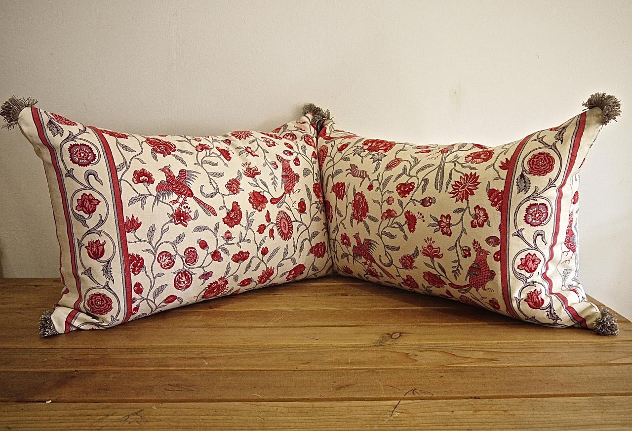 Pair of early 20th century French linen cushions printed with stylized exotic birds and animals in rasberry red and pink with grey meandering branches and leaves. Vintage French grey cotton fringing on each corner. Self-backed and slip-stitched