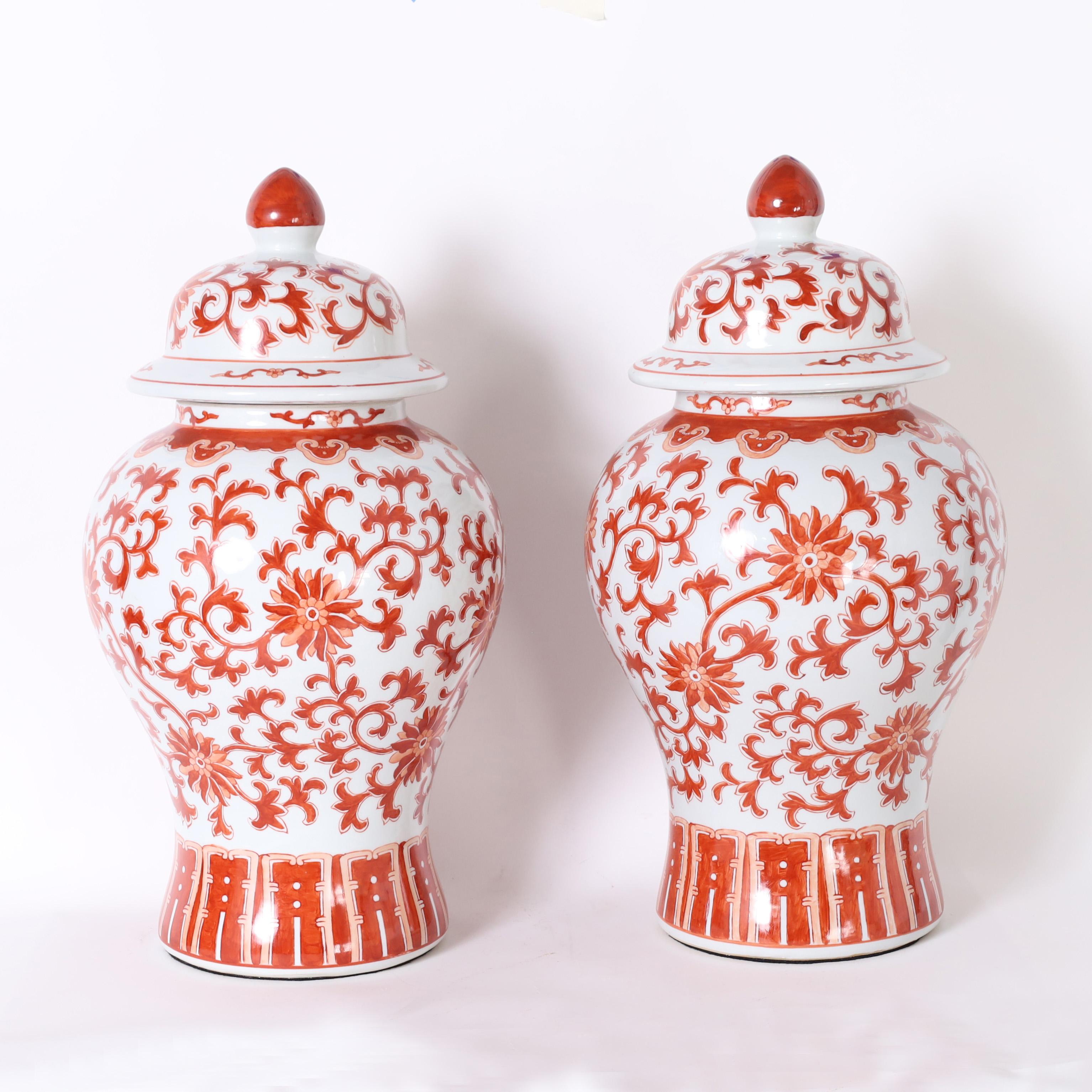 Standout pair of Chinese porcelain lidded urns with classic form hand decorated with flowers and leaves in orange and red.