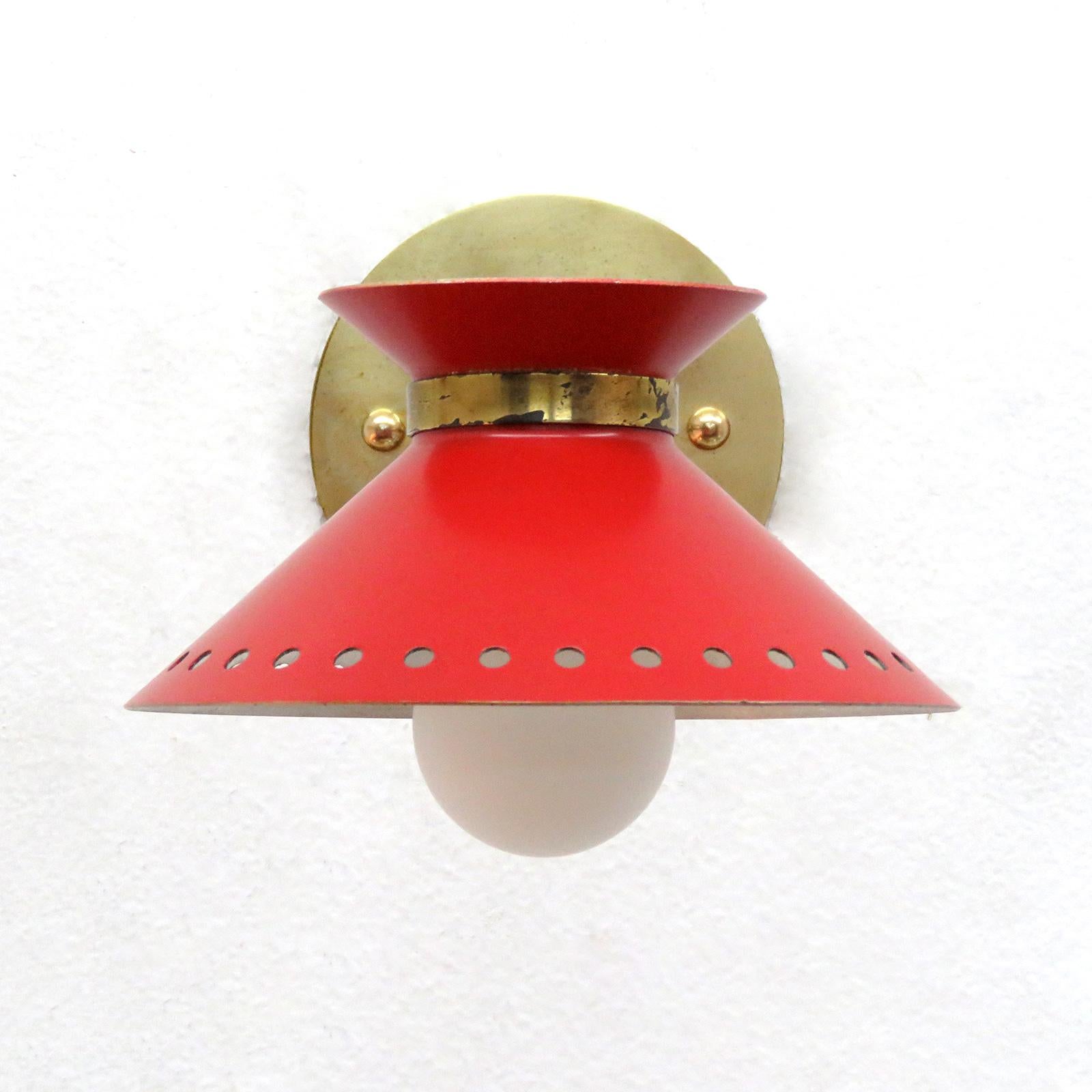 Wonderful pair of red enameled French double cone wall lights by Arlus, with pivoting shades on articulate brass arms, perforated along the bottom edge, wired for US standards, one E12 socket per light, max. wattage 75w, bulbs provided as a one time