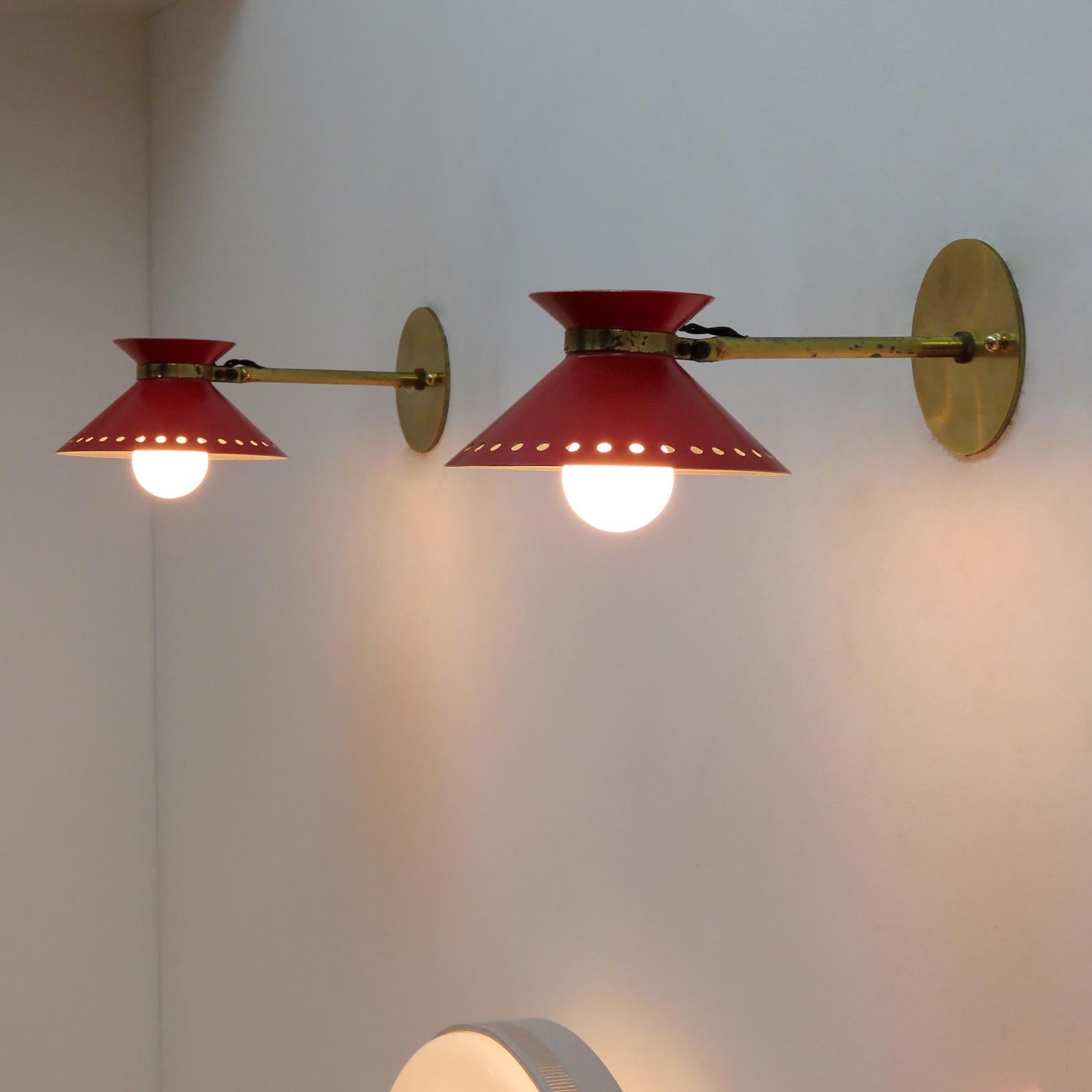 Wonderful pair of red enameled French double cone wall lights by Arlus, with pivoting shades on articulate brass arms, perforated along the bottom edge, wired for US standards, one E12 socket per light, max. wattage 75w or 3-7w LED equivalent, bulbs