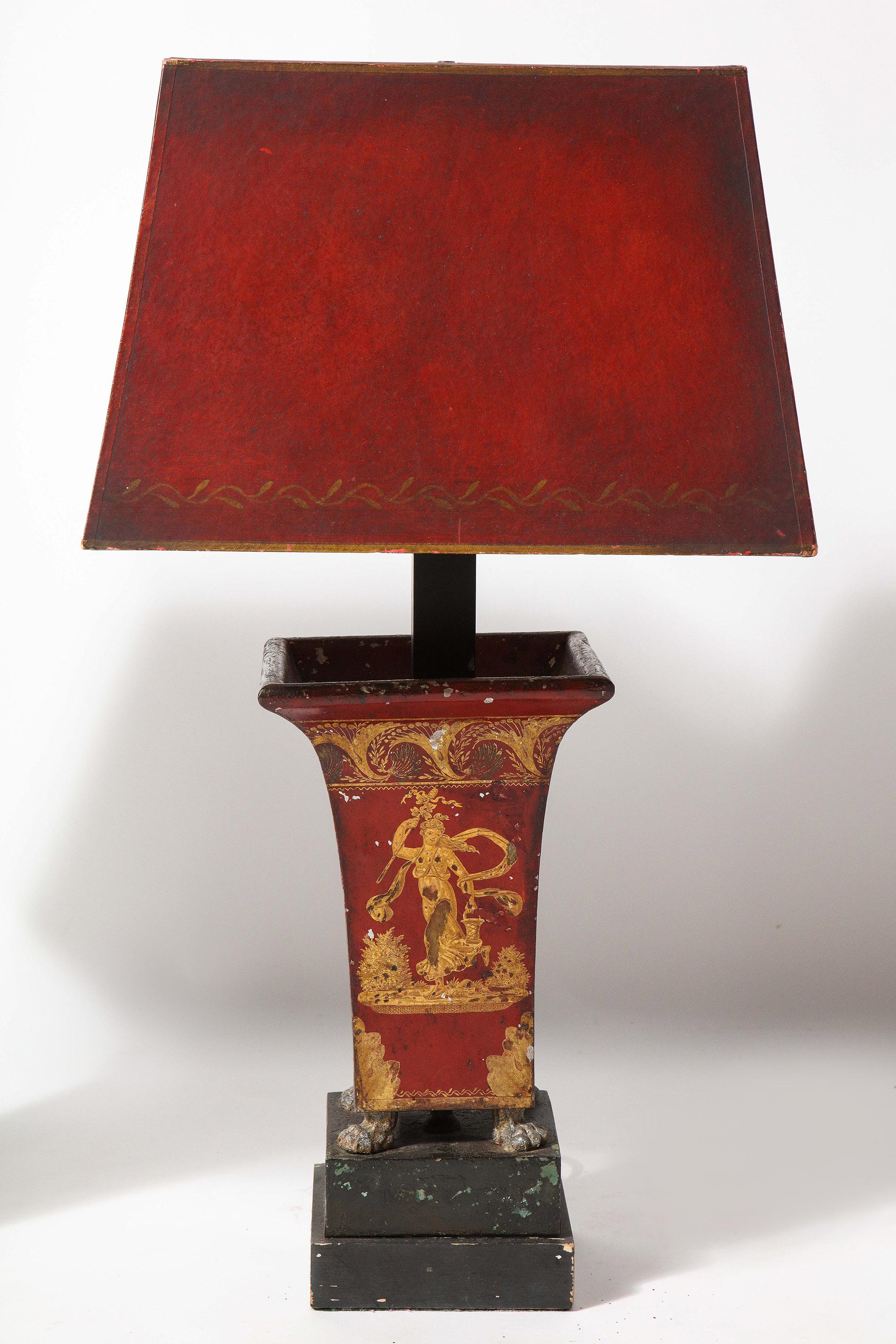 Pair of Empire red tole peinte cachepots mounted as lamps. Each with with classical figures and Empire decoration, raised on paw feet set on original plinth. Recently mounted as lamps with matching hand painted shades have been.