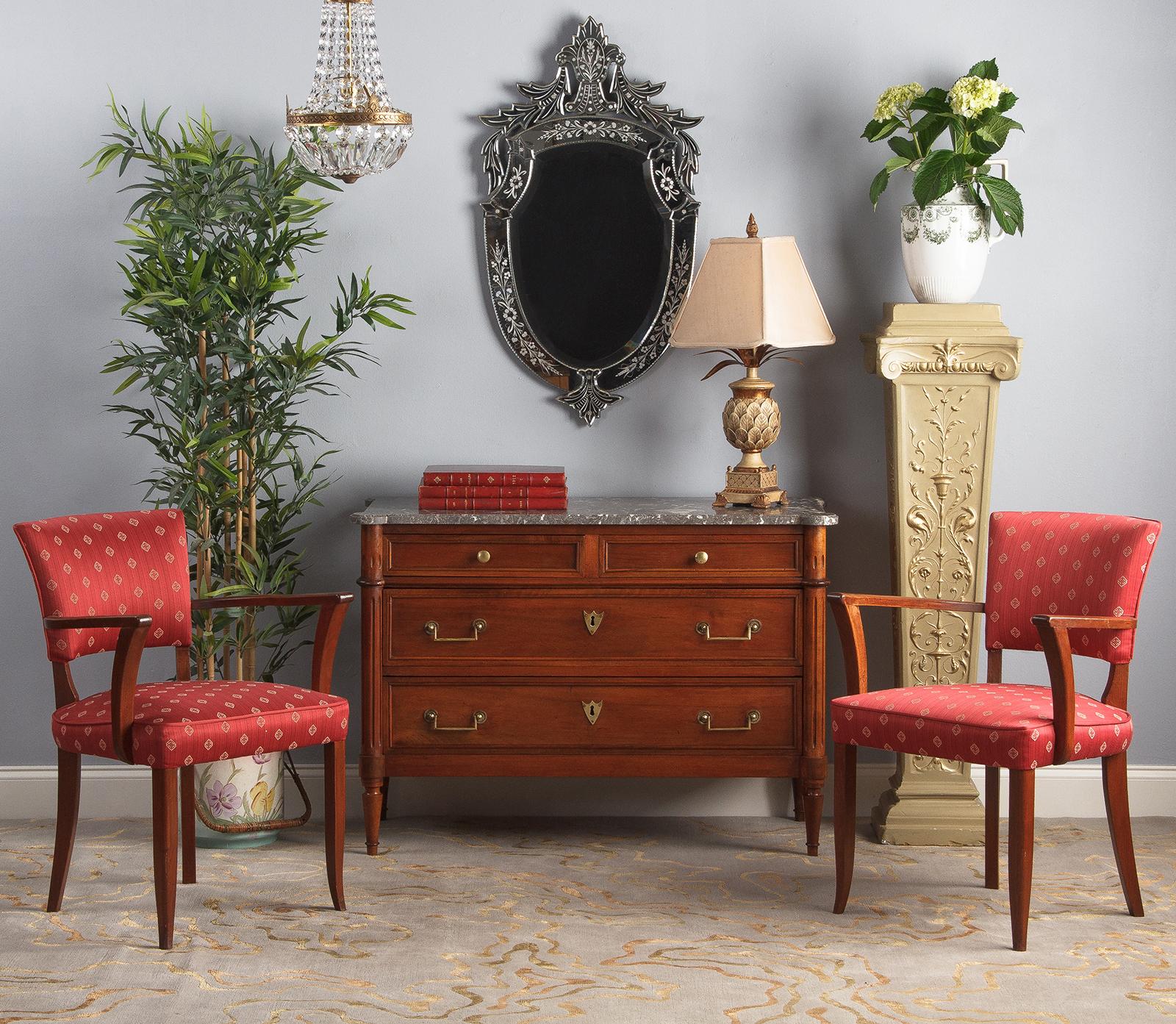 An outstanding pair of French bridge armchairs from the Art Deco period. Both armchairs have recently been re-upholstered in a patterned red fabric. The frames are stained beechwood with shapely curved front legs and armrests. This pair of bridge