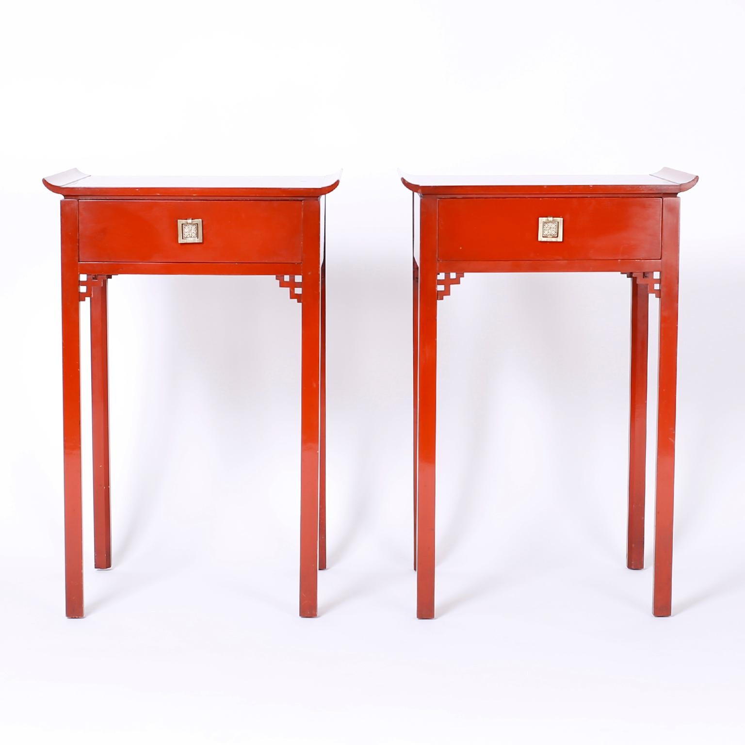 Pair of pagoda stands or tables lacquered in a distinctive Chinese red featuring tops decorated with hand painted chinoiserie scenes, Ming style brass hardware, Asian brackets and long elegant legs.