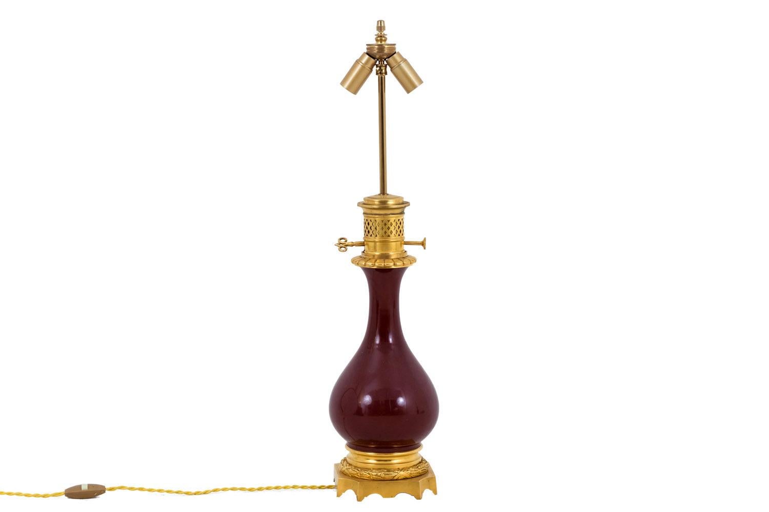 Pair of baluster shape red “sang-de-bœuf” (oxblood) porcelain lamps.
Chiselled and gilt bronze mount. High part with openwork motifs of grid and a gadroons frieze. Square shape base with eight legs and scalloped edges, topped by a ribboned laurel