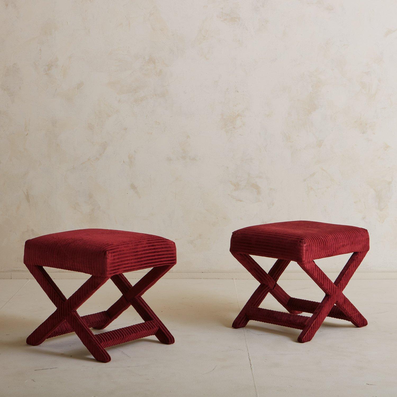 A pair of vintage square ottomans with x-bases and beautiful stretcher details. These pieces retain their original red fabric with subtle textured stripes. Two pairs available; priced per pair.